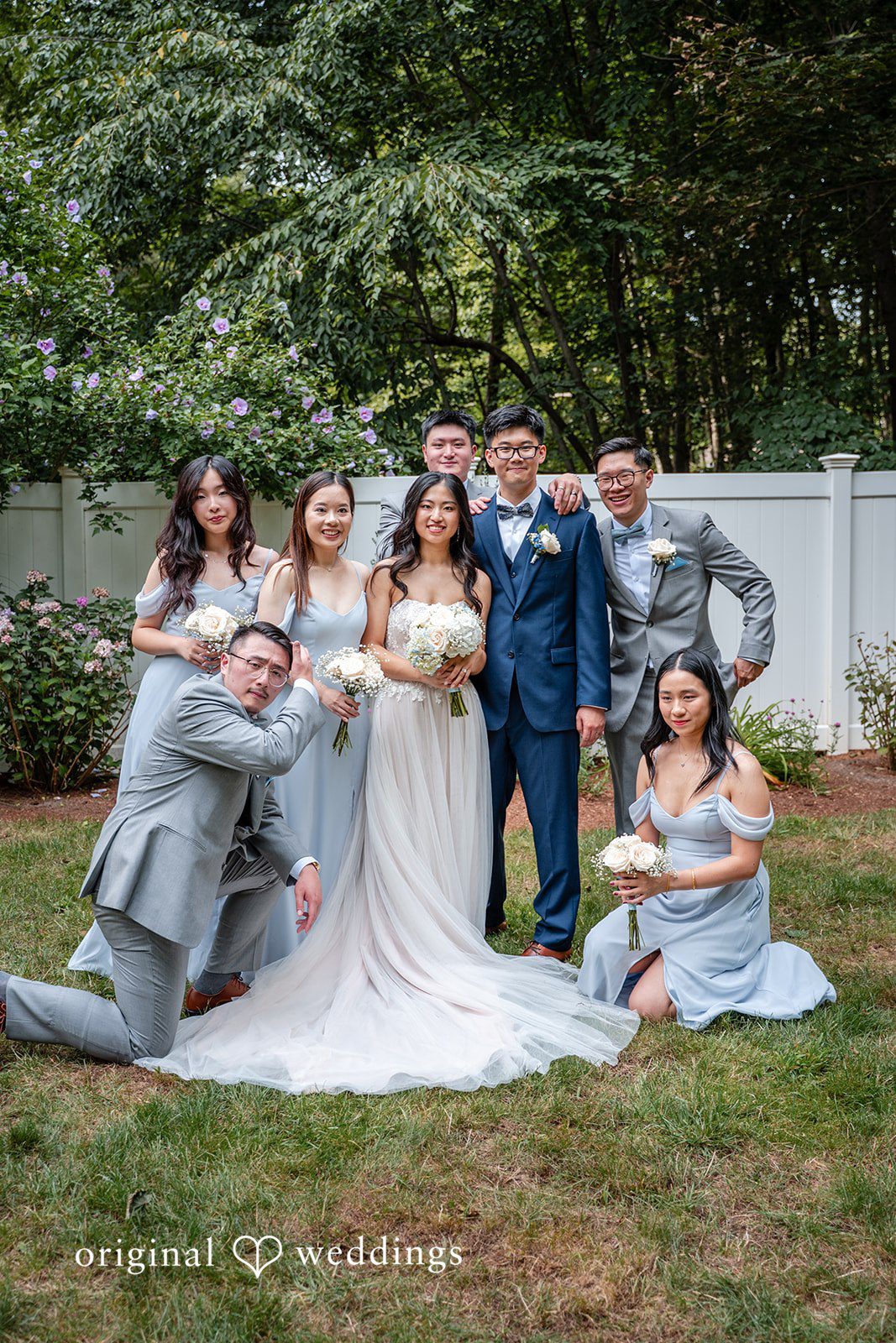 Wedding guests posing together on a grassy lawn with trees in the background.
