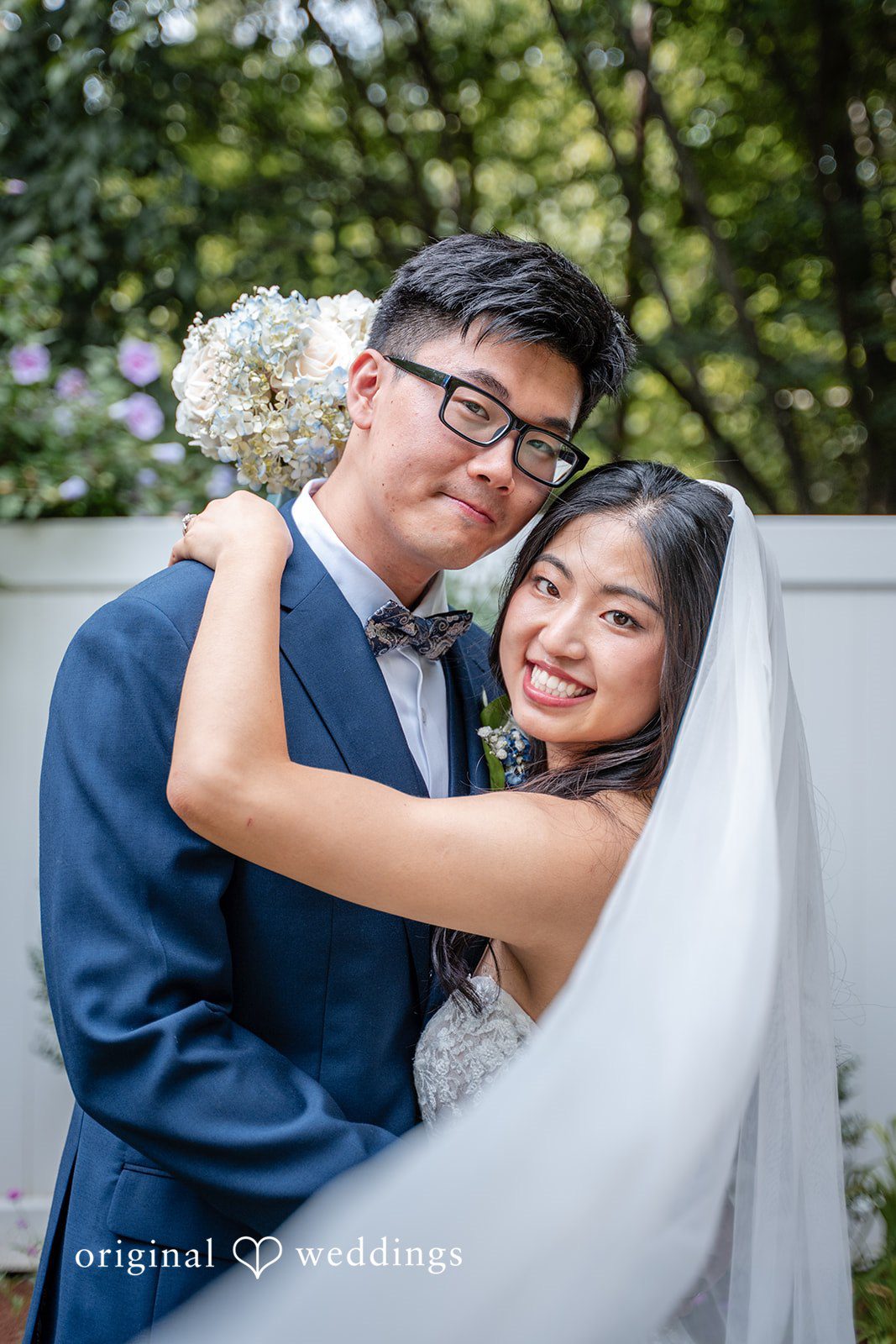 Groom in a blue suit hugging a bride wearing a long white wedding veil.