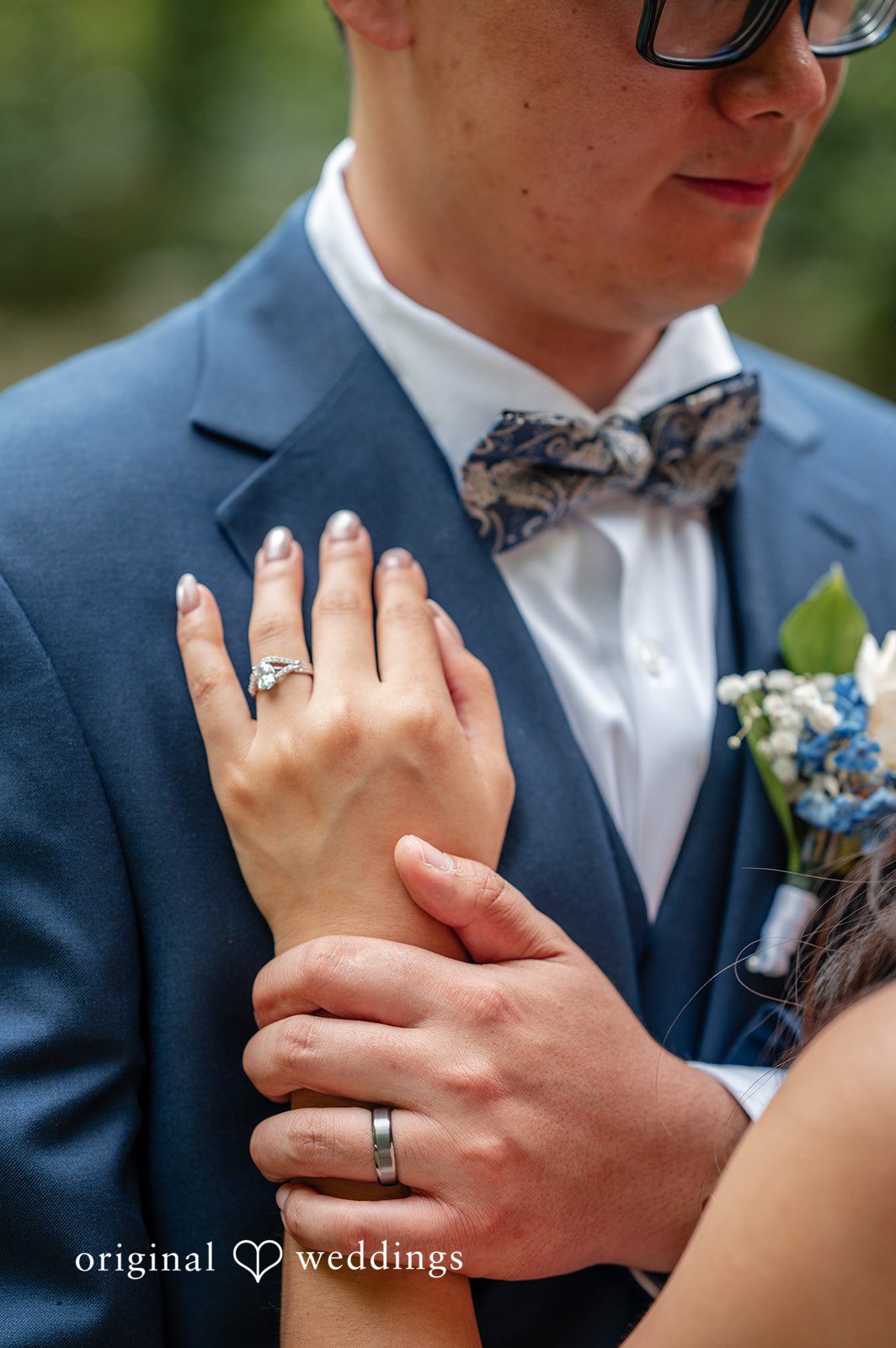 Close-up of a groom's hands clasped together over his grey suit and bowtie.