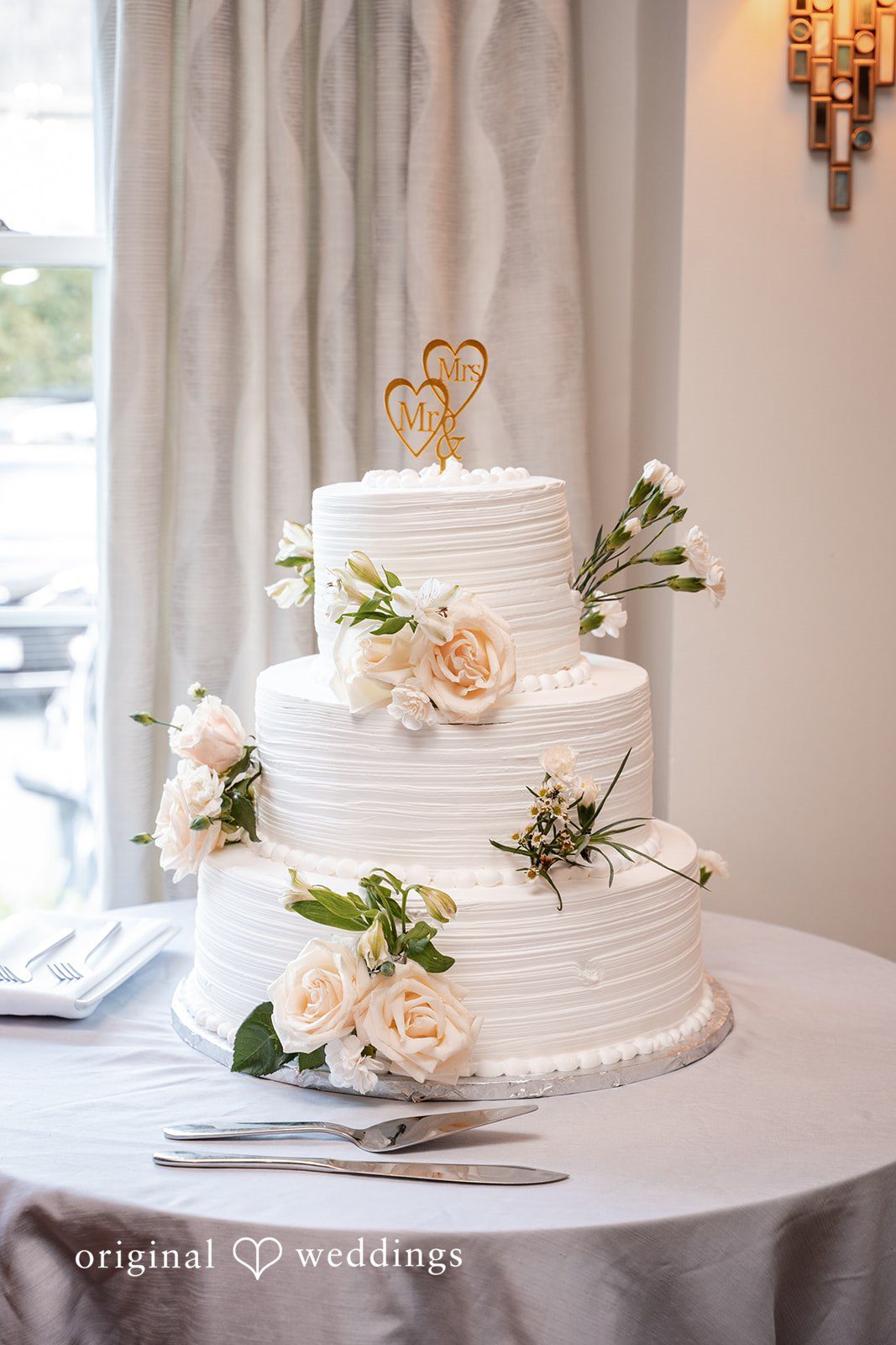 Three-tiered white wedding cake adorned with delicate green foliage.