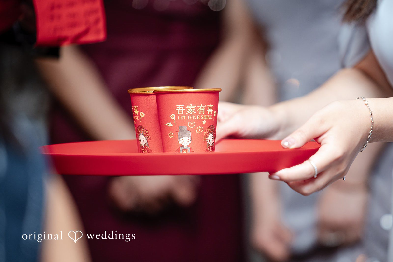 Close-up of hands holding a red tray with a cup during a traditional tea ceremony.