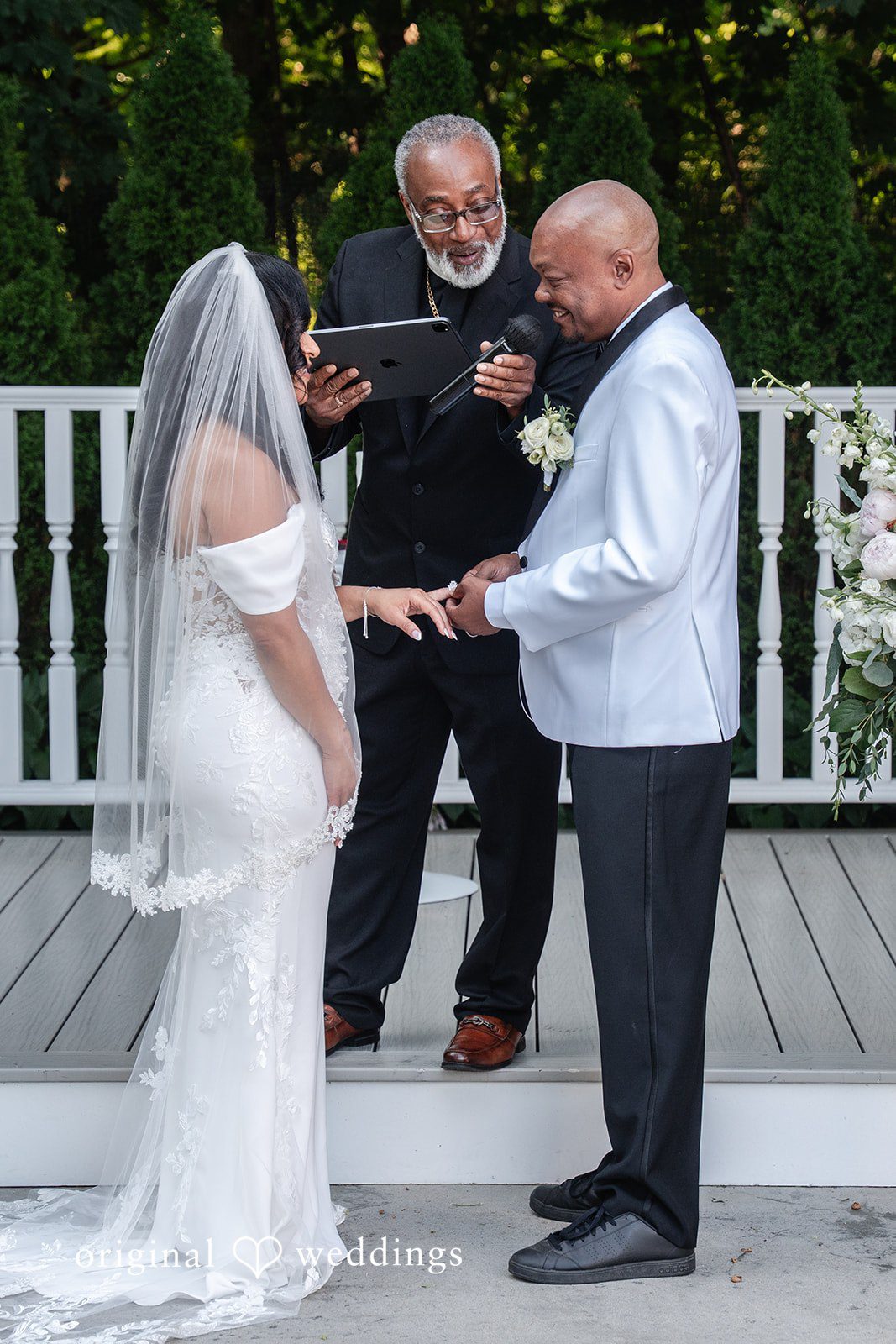Melissa + Walter A wedding ceremony in progress, showing the bride, groom, and an officiant reading from a book.