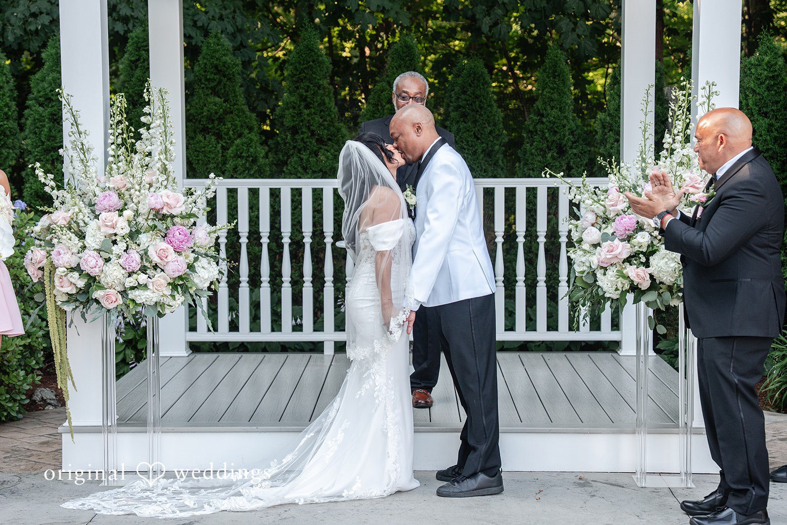 Melissa + Walter A bride and groom standing hand-in-hand under a floral wedding archway.