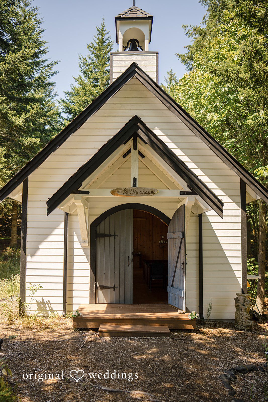 Jade + Nicholas A small white chapel with dark trim surrounded by green trees.
