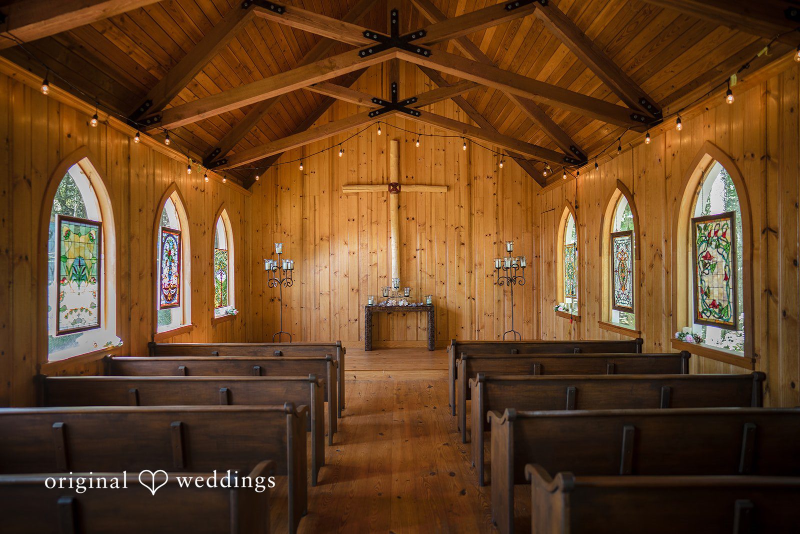 Jade + Nicholas The wooden interior of a church showing rows of pews leading to the altar.