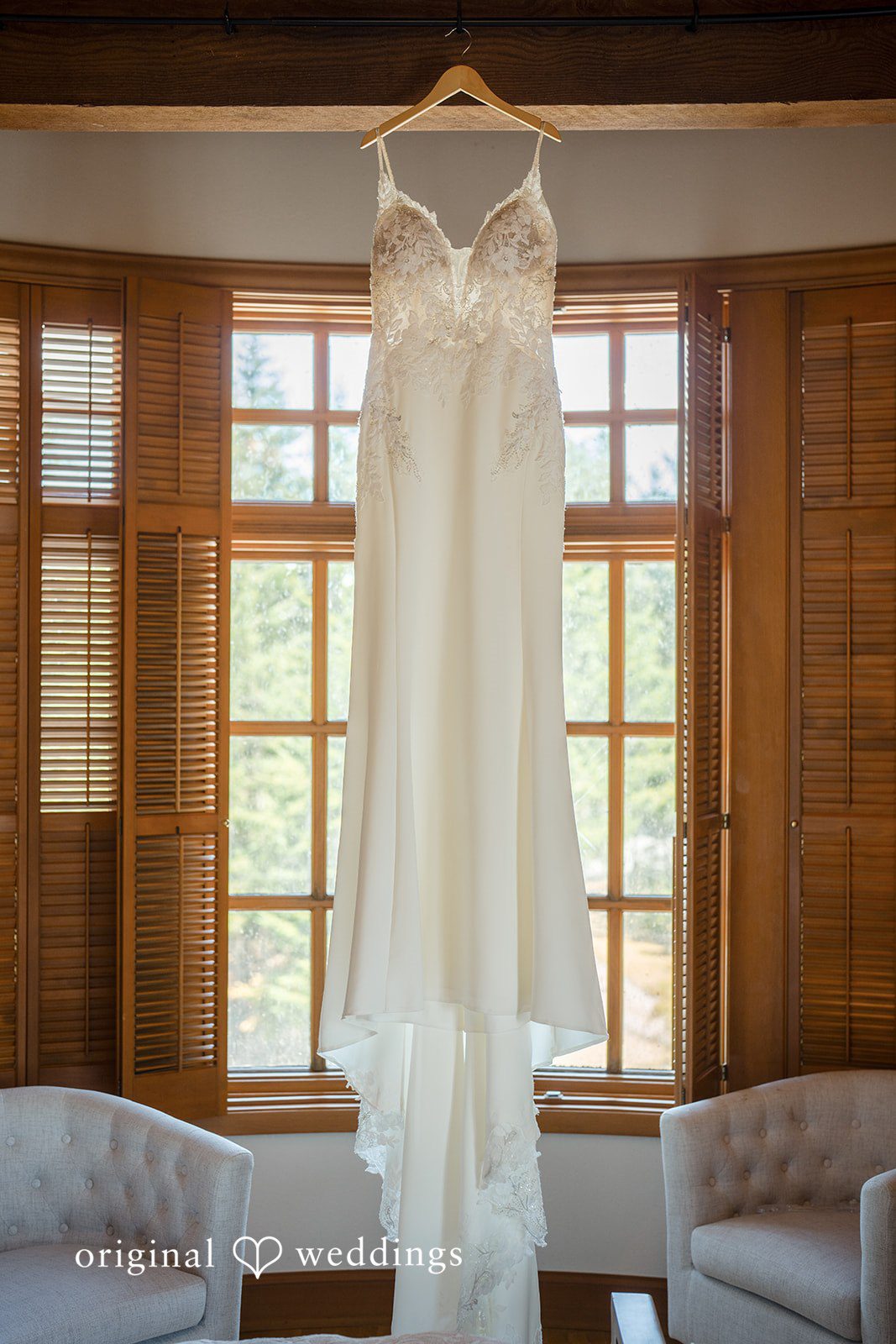 Jade + Nicholas A long white wedding dress hanging in front of a wooden window pane.