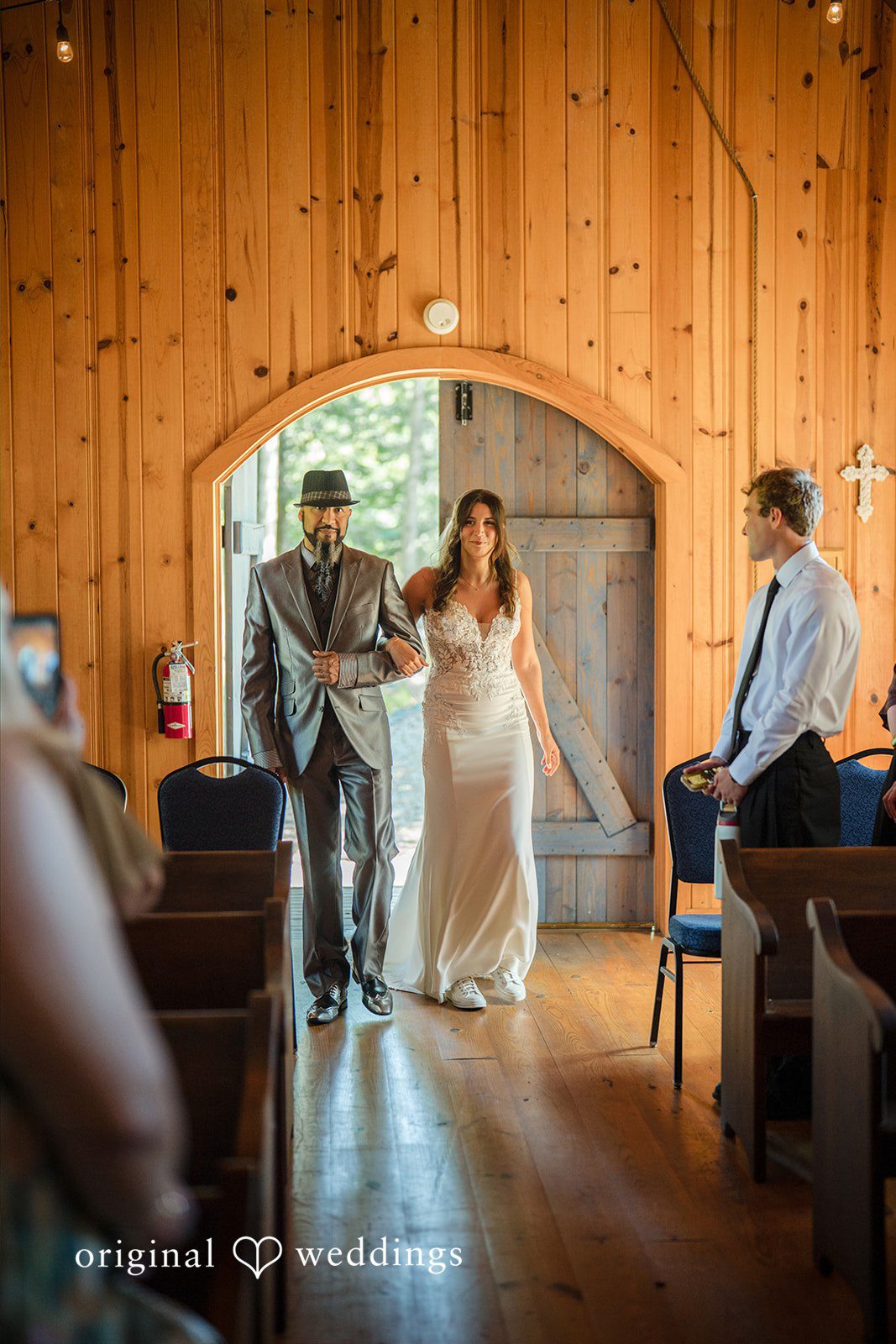 Jade + Nicholas A bride and an older man in a grey suit walk arm-in-arm down a church aisle.
