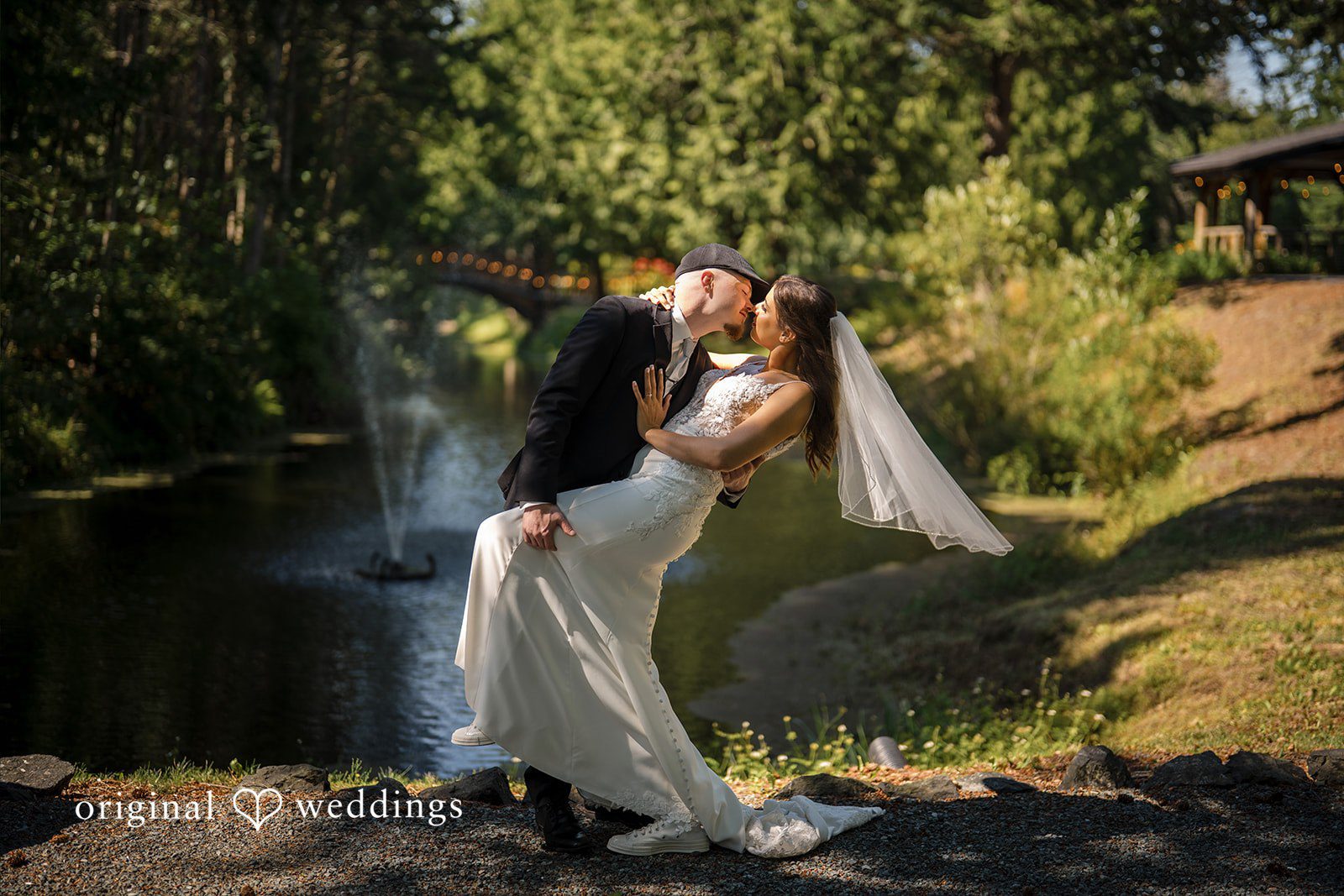 Jade + Nicholas A bride and groom dipping and kissing on a path surrounded by trees.