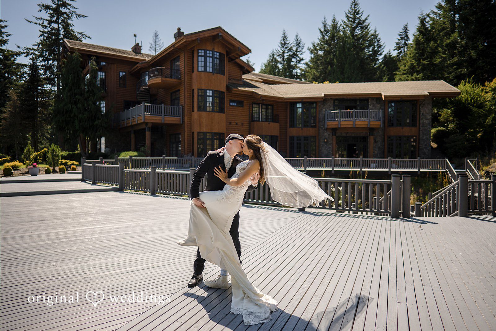 Jade + Nicholas A bride and groom sharing a dip kiss on a paved walkway outside a large building.