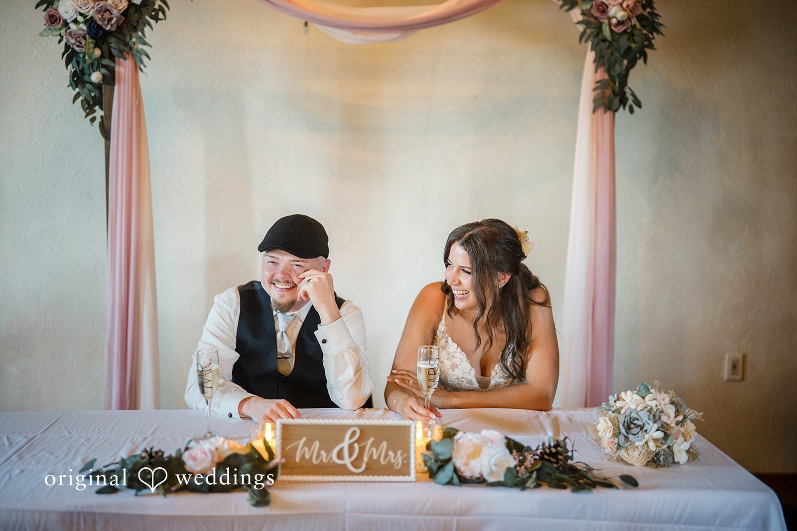 Jade + Nicholas Couple sitting behind a decorated head table during a reception event.