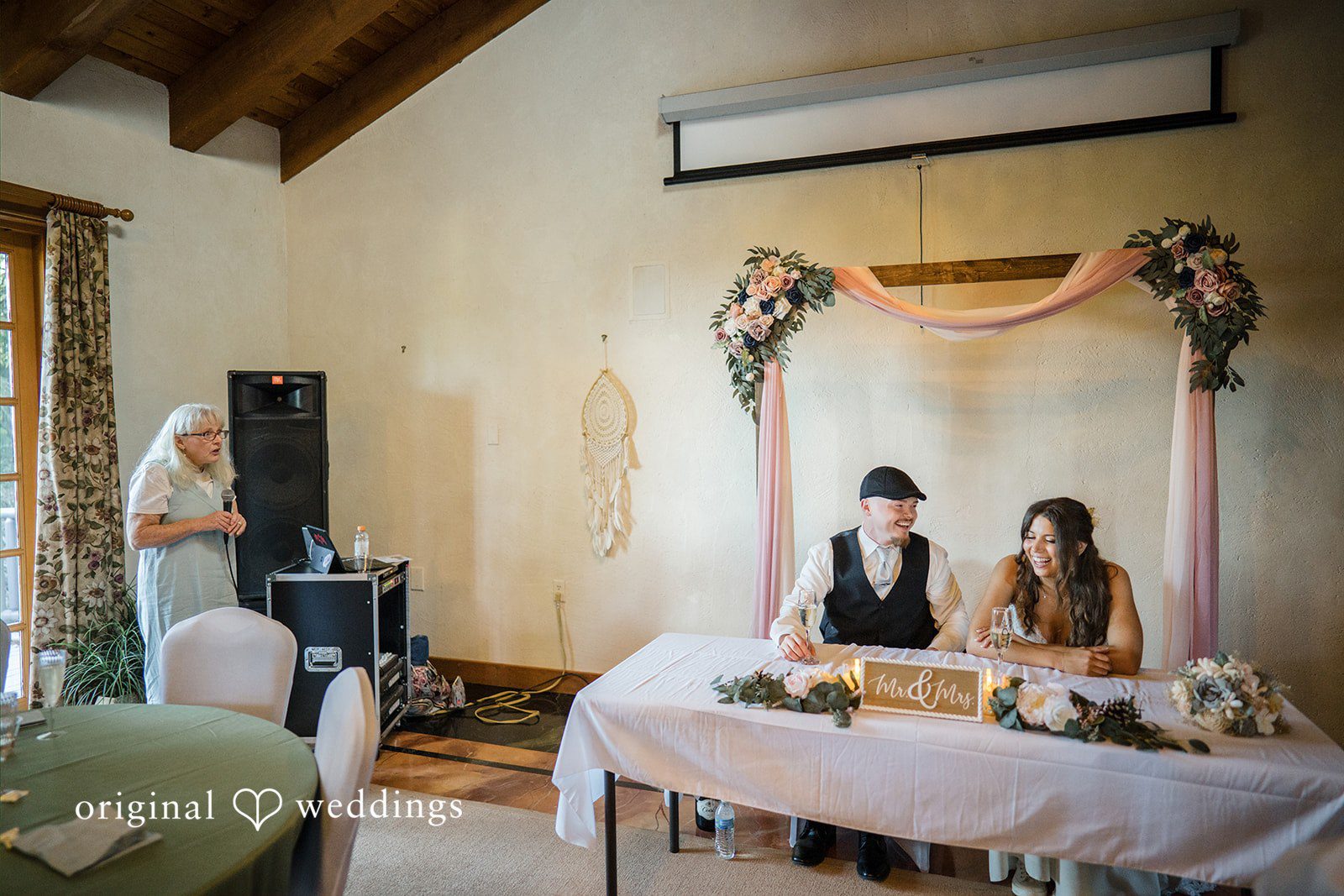 Jade + Nicholas A wedding head table setup inside a room with guests seated in the background.