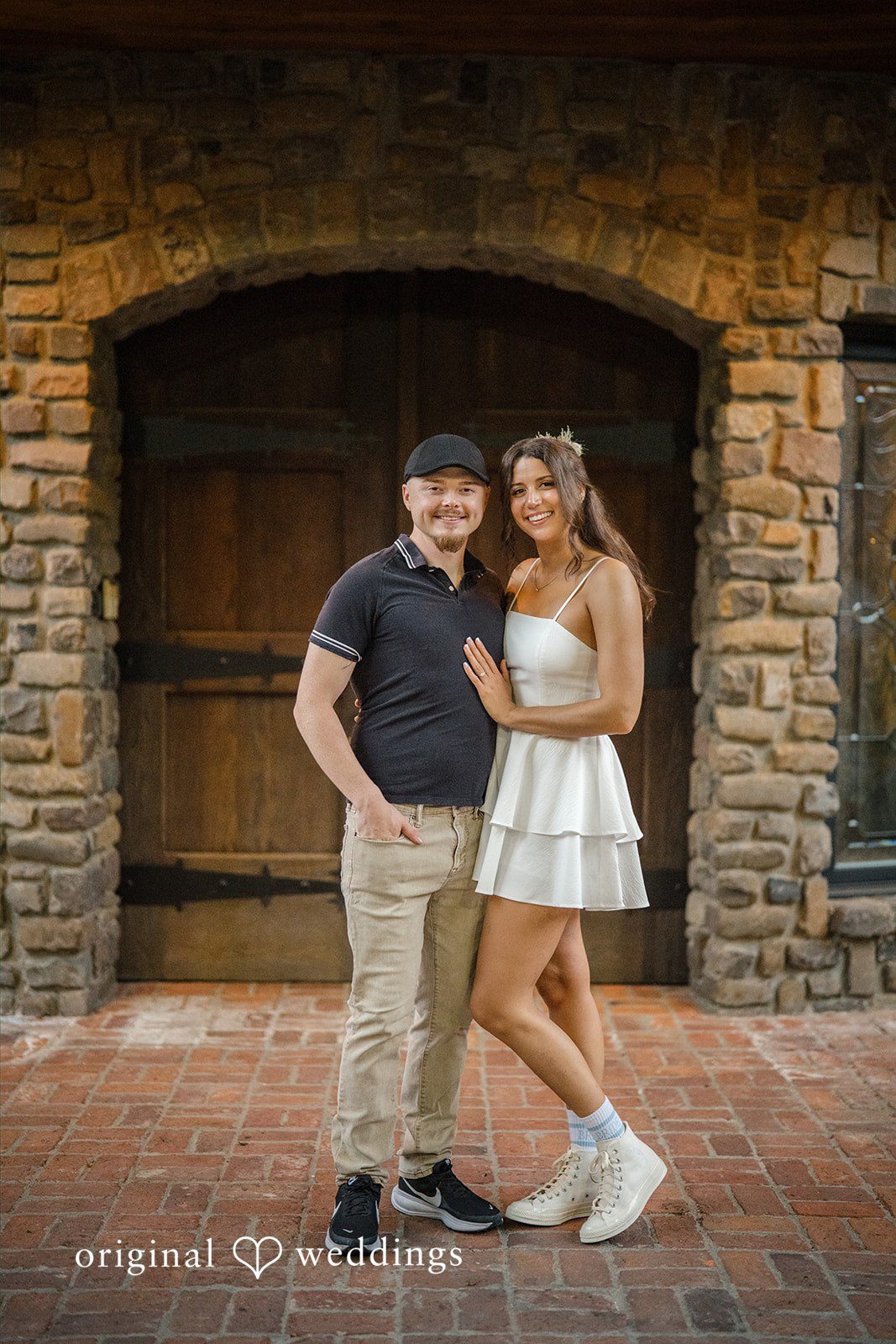 Jade + Nicholas Couple posing closely together in front of a stone and wood building wall.