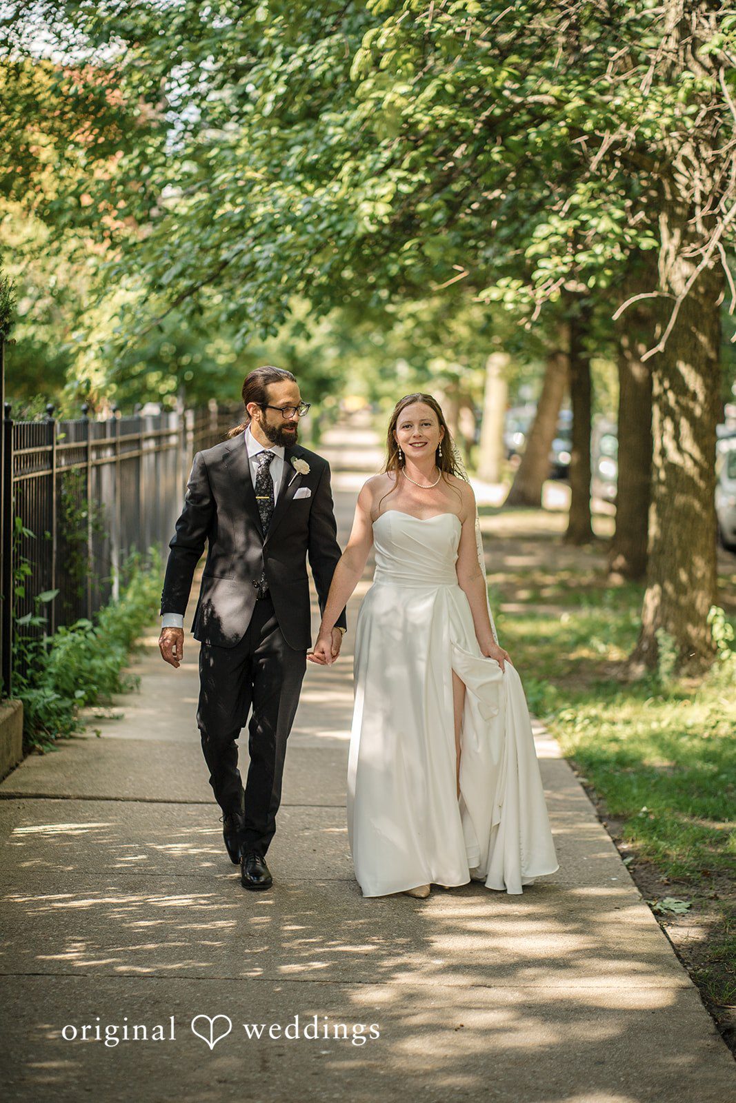 Kimberly + David Bride and groom holding hands and walking along a sunny outdoor path.