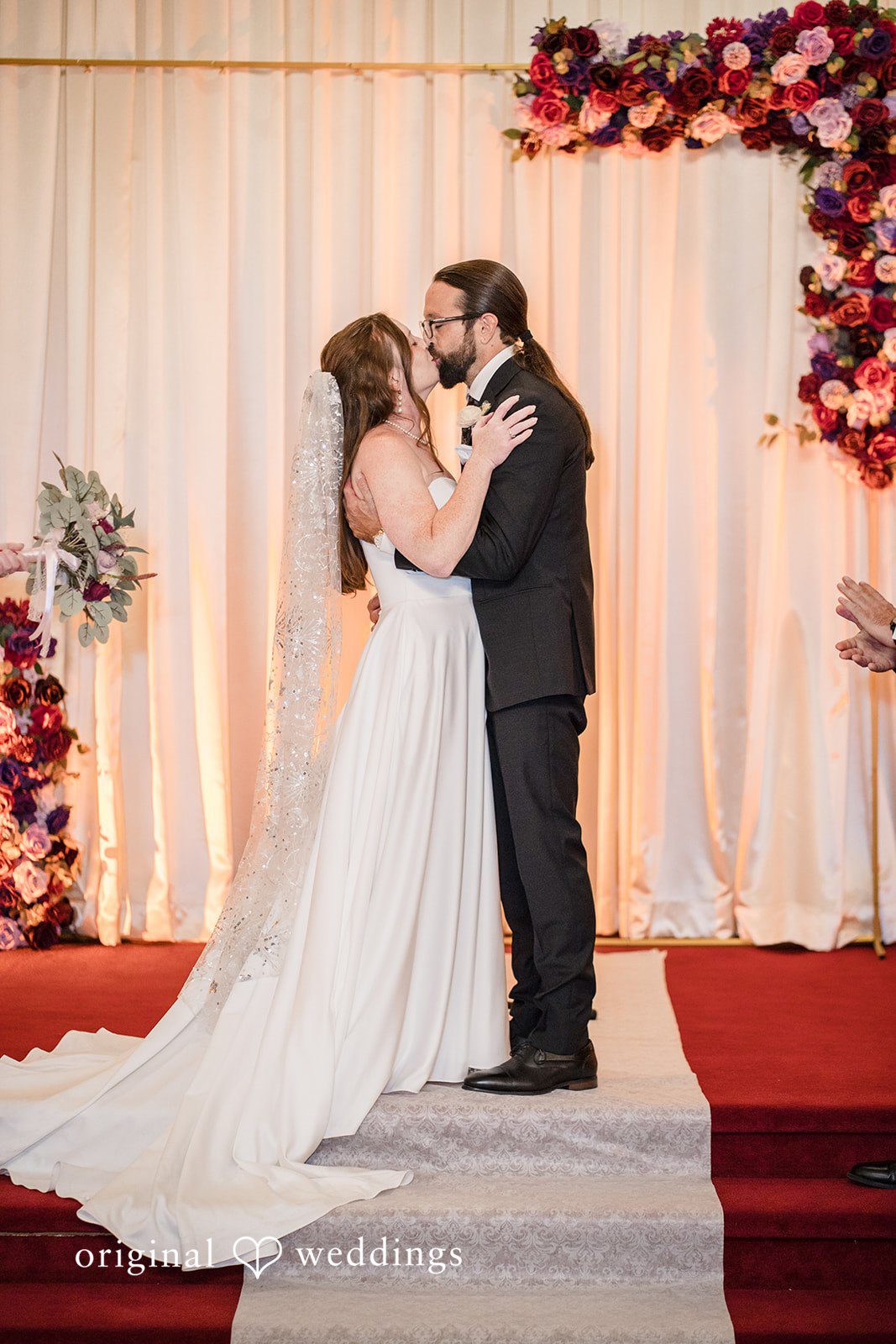 Kimberly + David Newlyweds embracing under a colorful floral wedding arch.