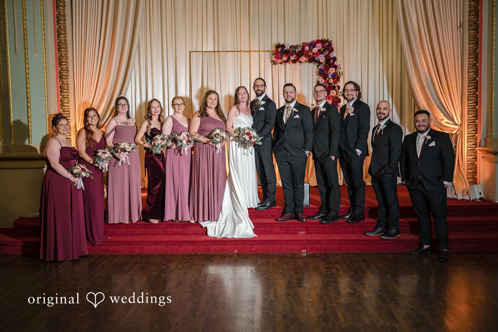 Kimberly + David Entire bridal party standing together on a red carpet stage indoors during the ceremony.