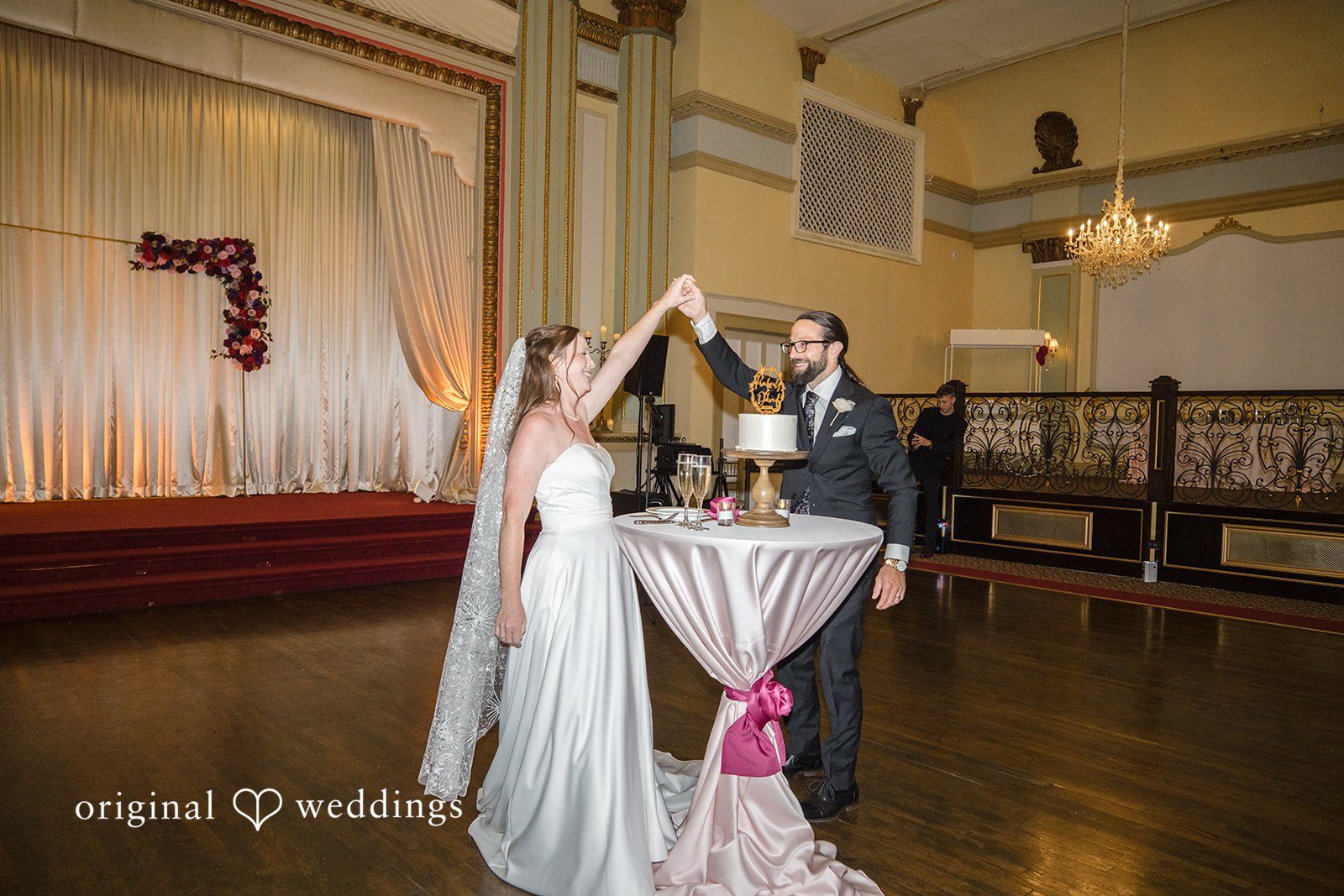 Kimberly + David Bride and groom holding hands next to their single-tier wedding cake on a cocktail table.