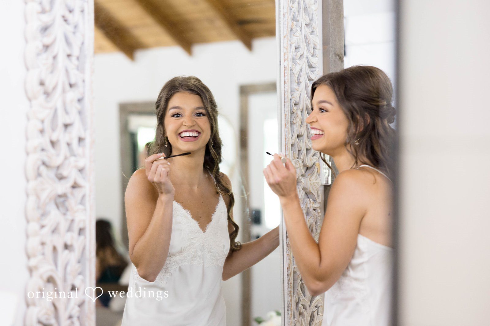 Bride in light dresses fix their makeup in front of a mirror.
