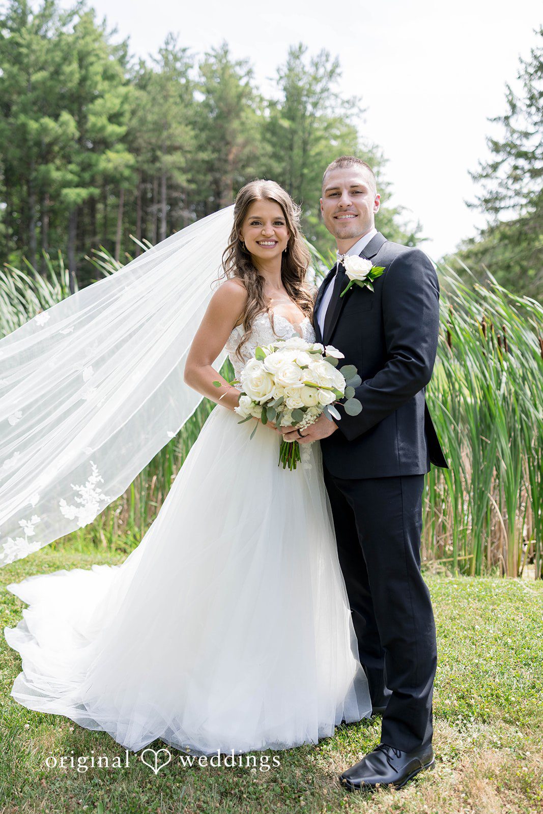 A bride and groom hold hands while standing on a grassy field.
