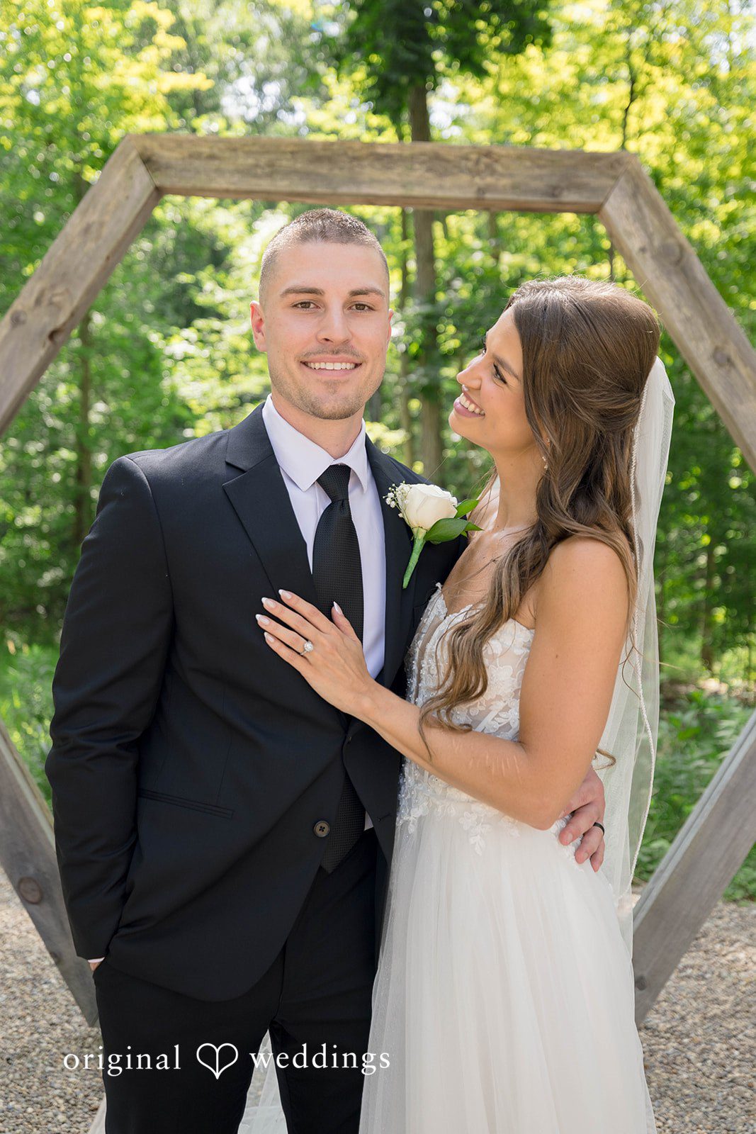 A groom in a black suit looks towards a bride in a white gown.