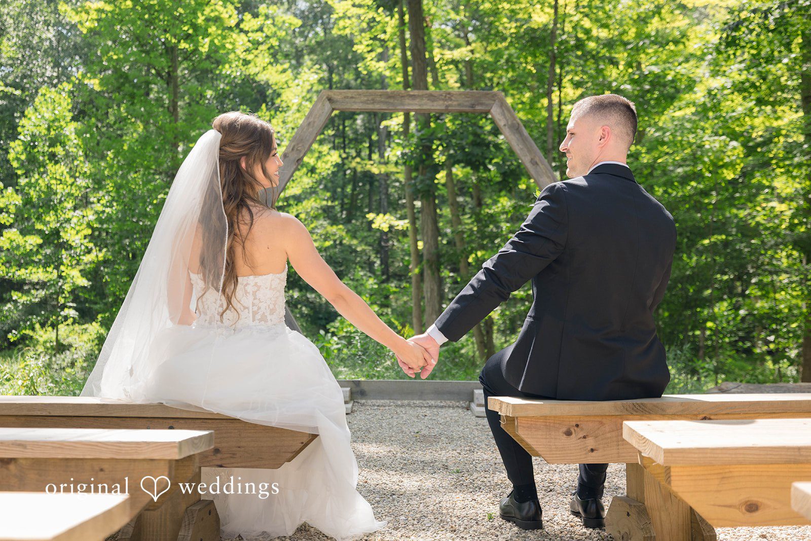 A bride and groom hold hands while sitting on a wooden bench