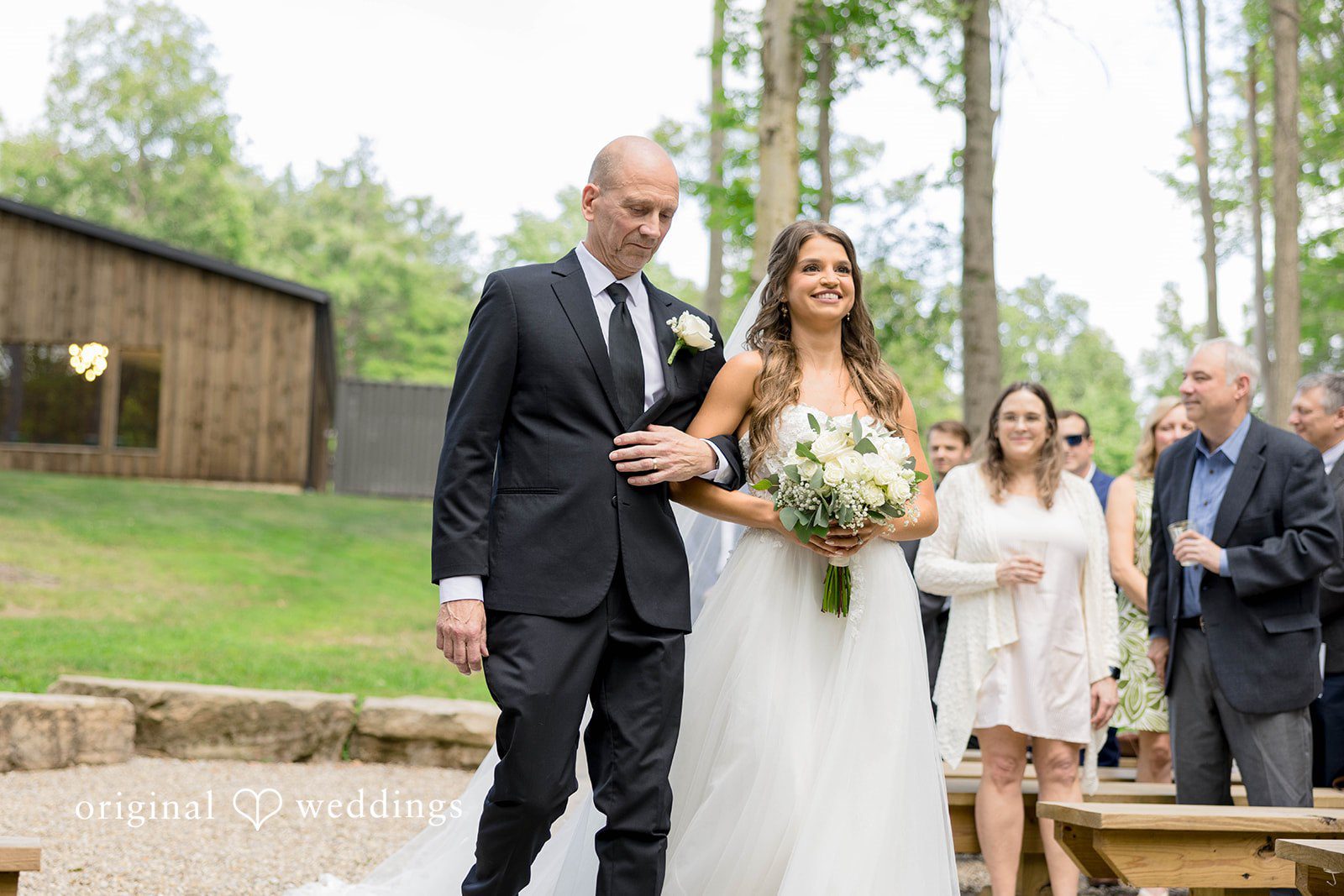 A bridal party walks together down a path near a rustic building.