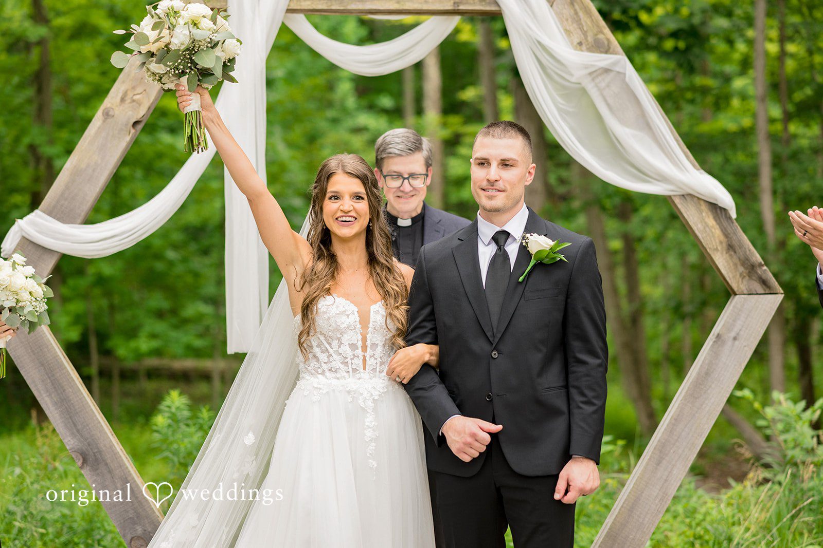 A bride and groom stand before a wooden geometric arbor structure.