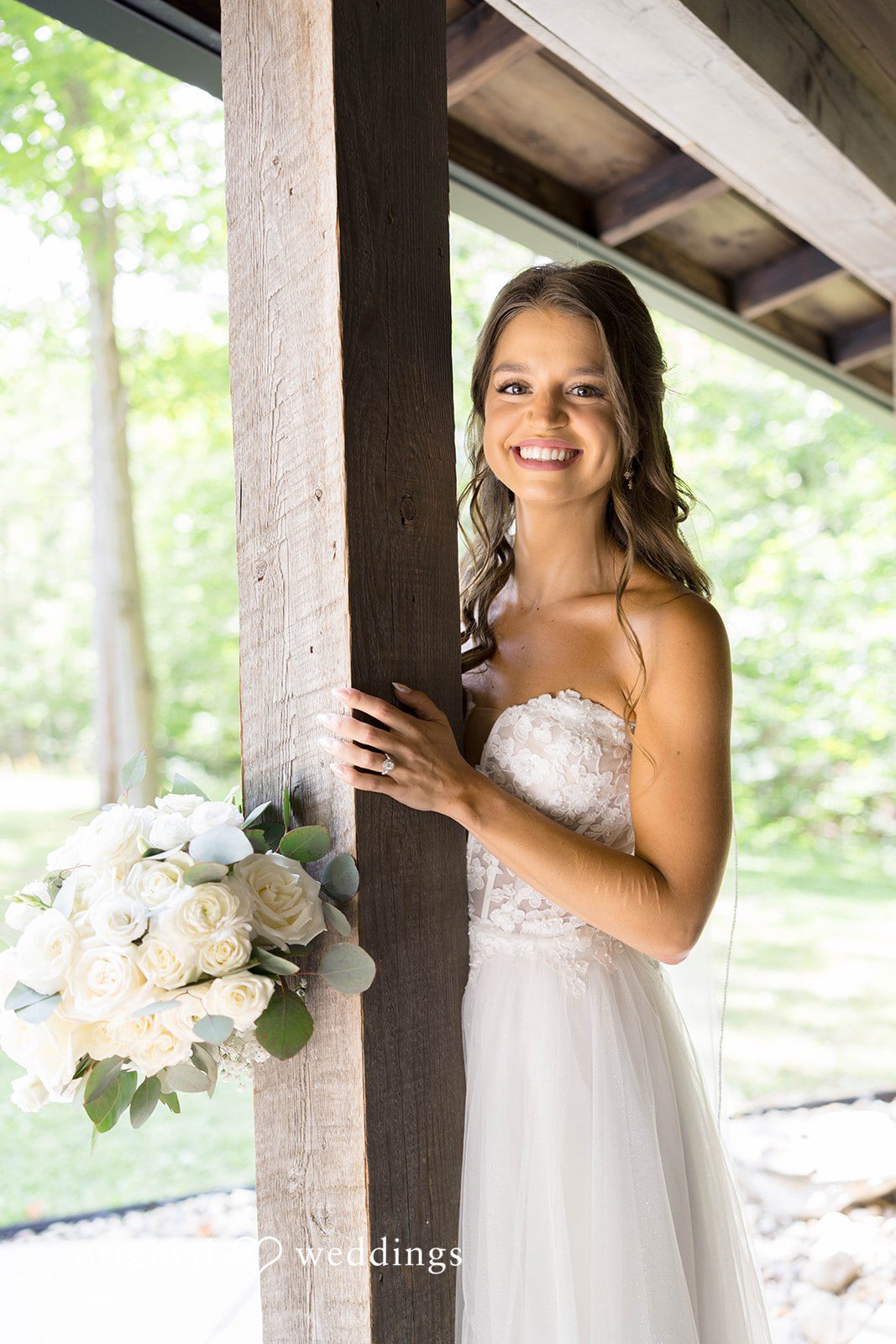 A bride poses for a portrait while leaning against a rustic wooden wall.