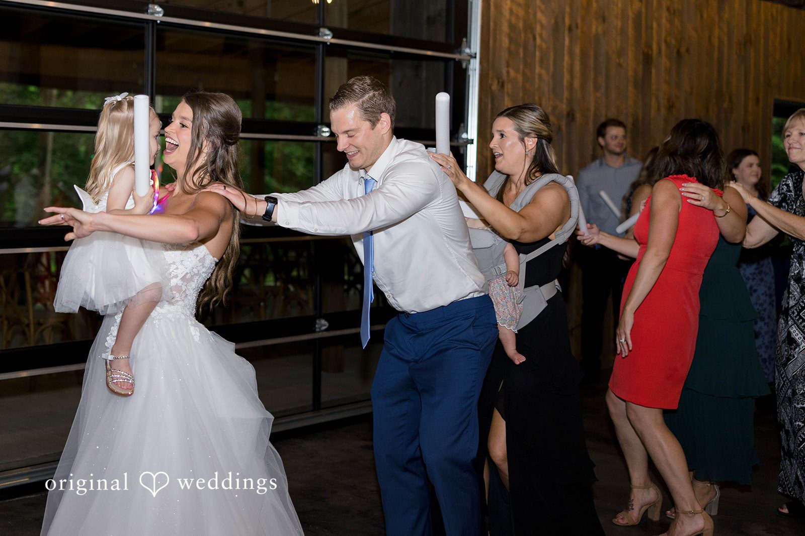 A group of wedding guests form a conga line while dancing at a wedding reception.