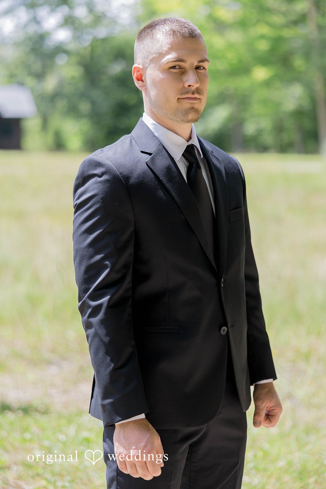 A man in a dark formal suit poses for a portrait.