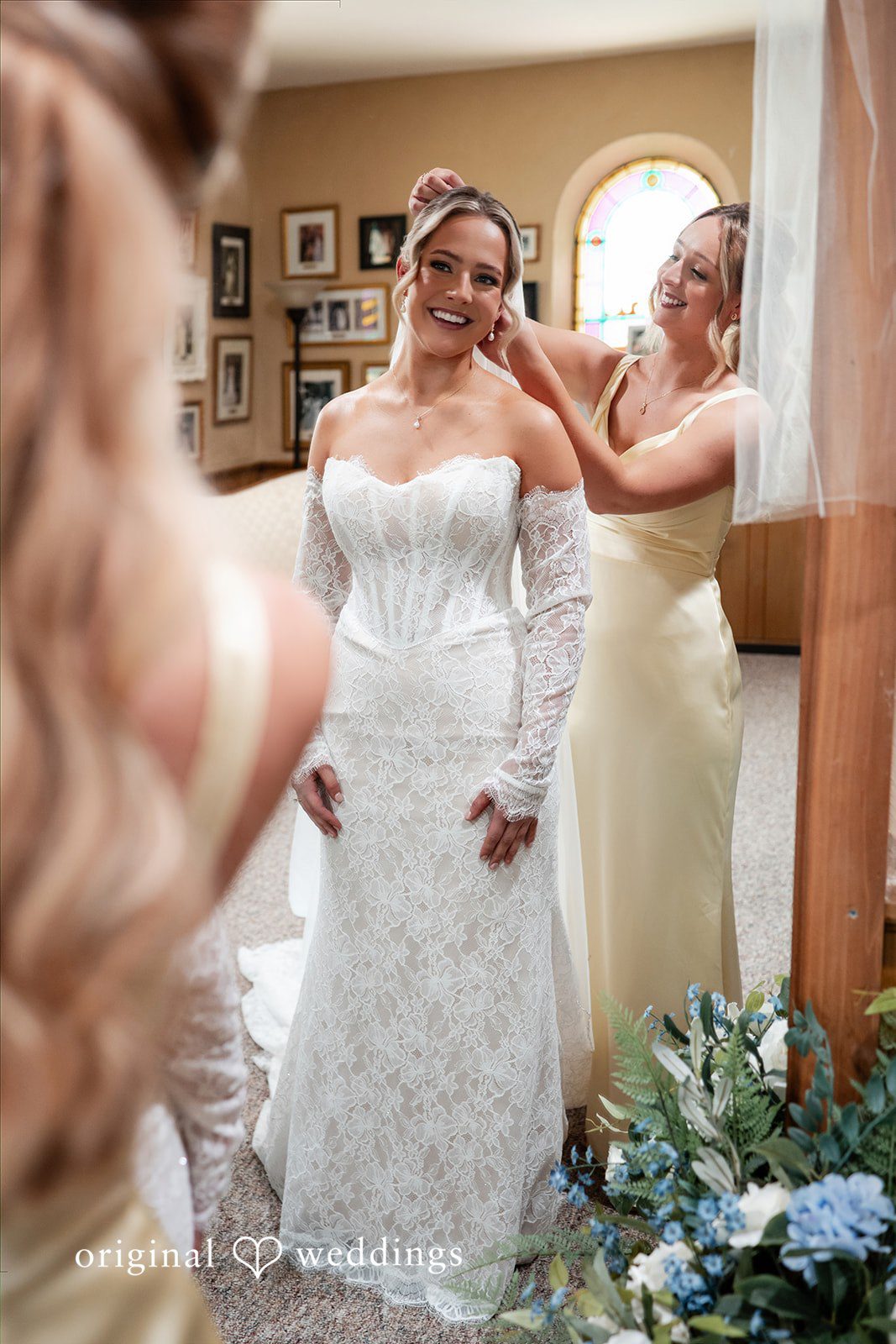 A bride looks at her reflection in a large mirror while getting ready.