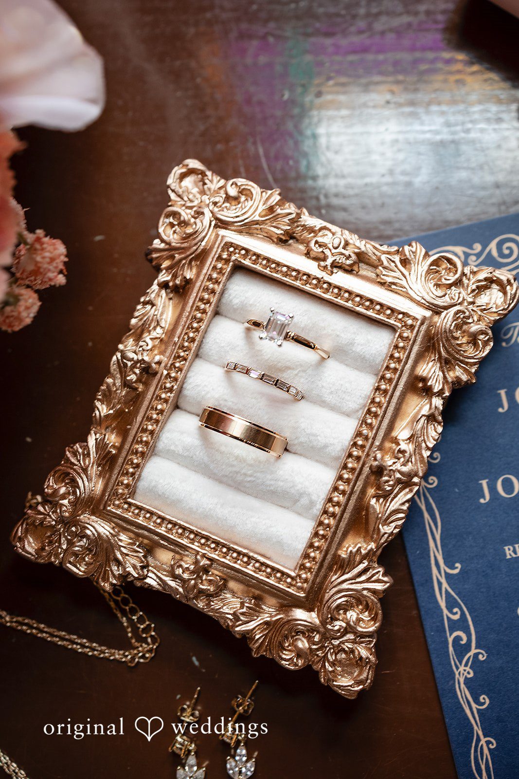 Wedding rings rest inside an ornate, gold-framed vintage ring box.