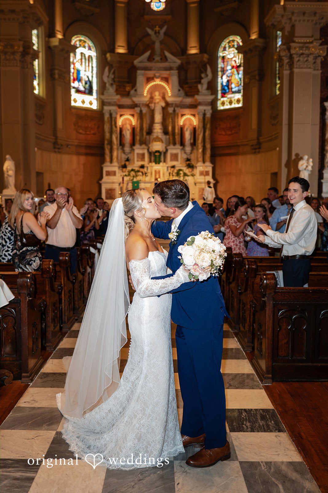 A bride and groom walk together down a church aisle lined with guests.