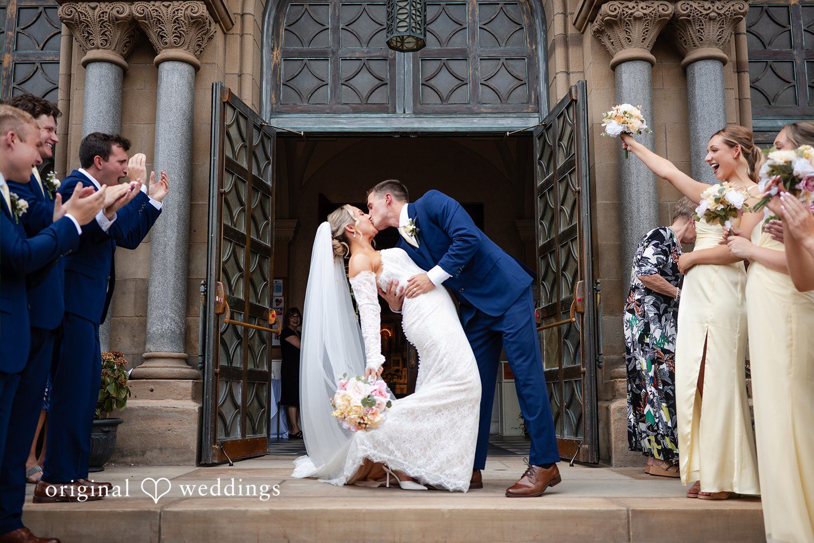 A bride and groom kissing and stand close together near the open doorways of a large church.