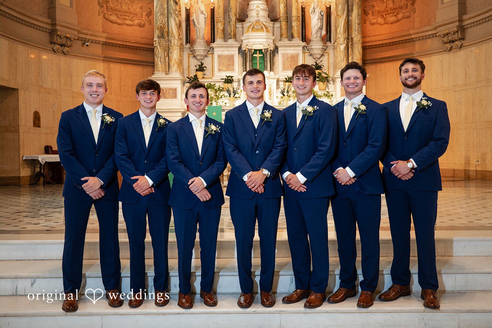 Groom and groomsmen in matching dark blue suits stand side-by-side.
