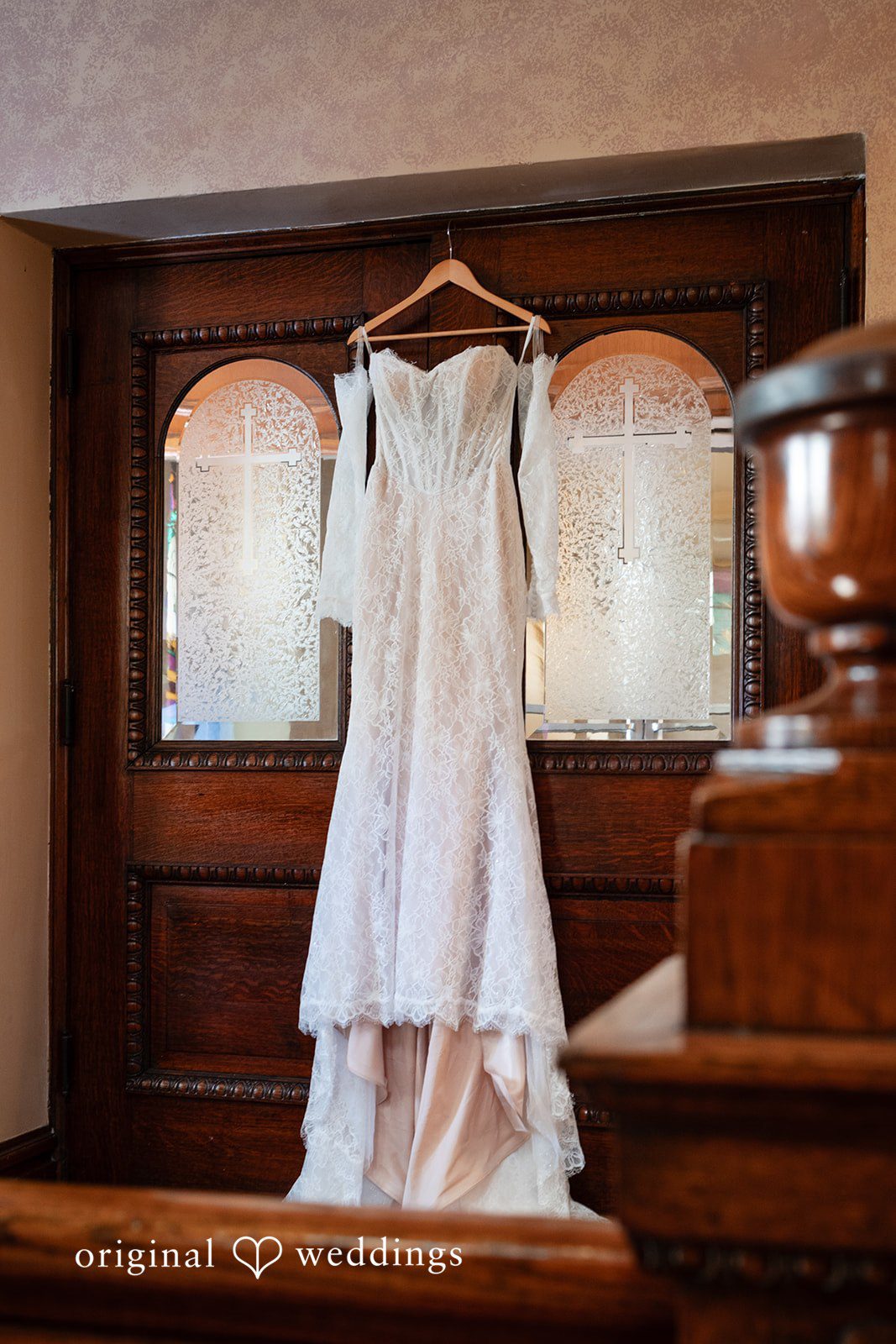 A white lace wedding gown hangs inside a wooden wardrobe frame.