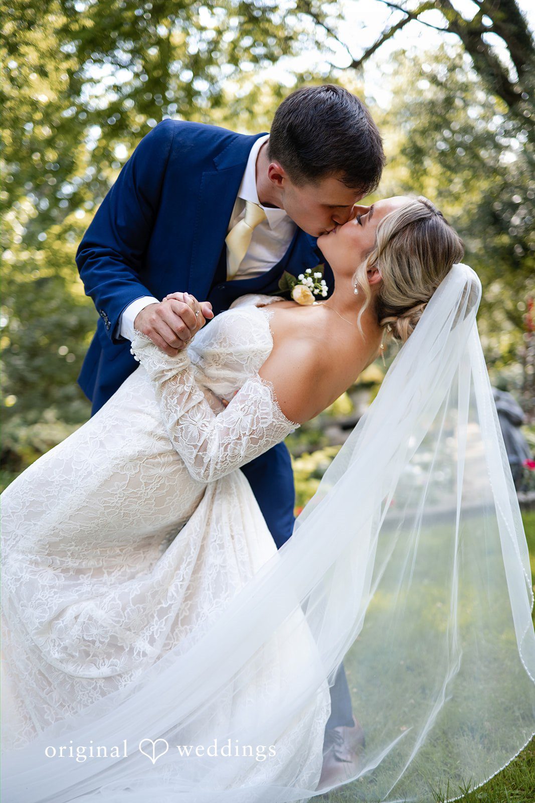 A groom dips his bride backwards during a romantic moment on a lawn.