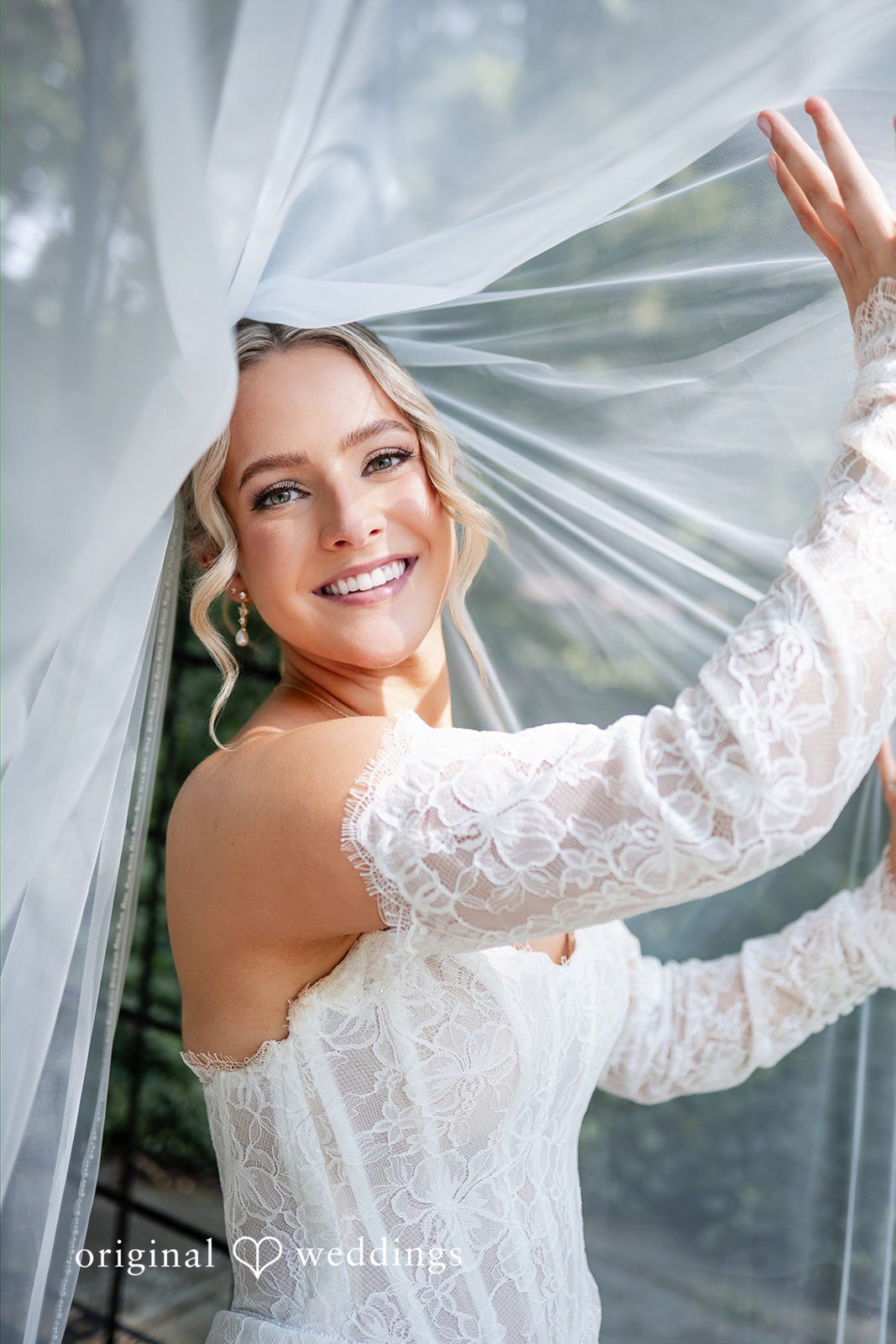 A smiling bride poses beneath a translucent white veil that frames her face.