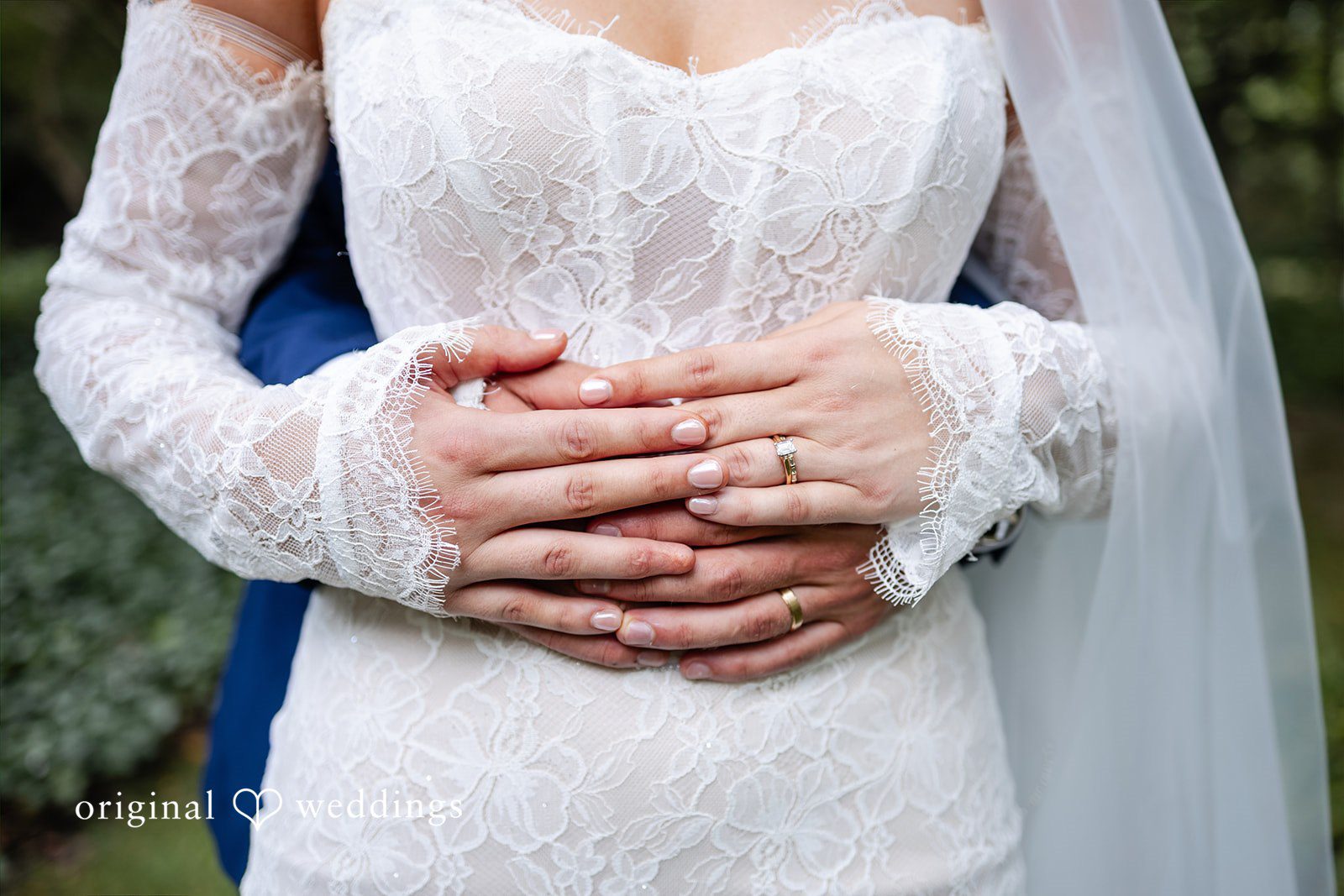 A close-up view focuses on a groom's hands wrapped gently around his bride's waist.