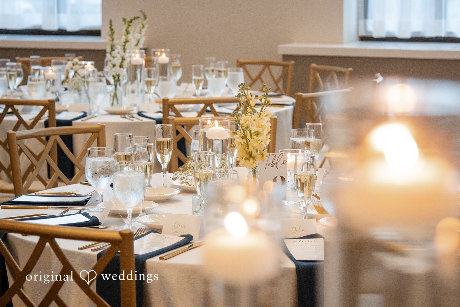 A reception table setting features glowing candles and glass drinkware.