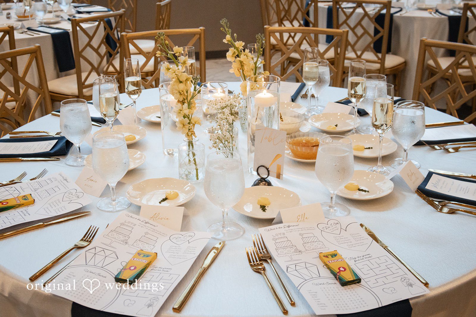 A beautifully arranged round dinner table is set with plates, cutlery, and gold-trimmed glasses.