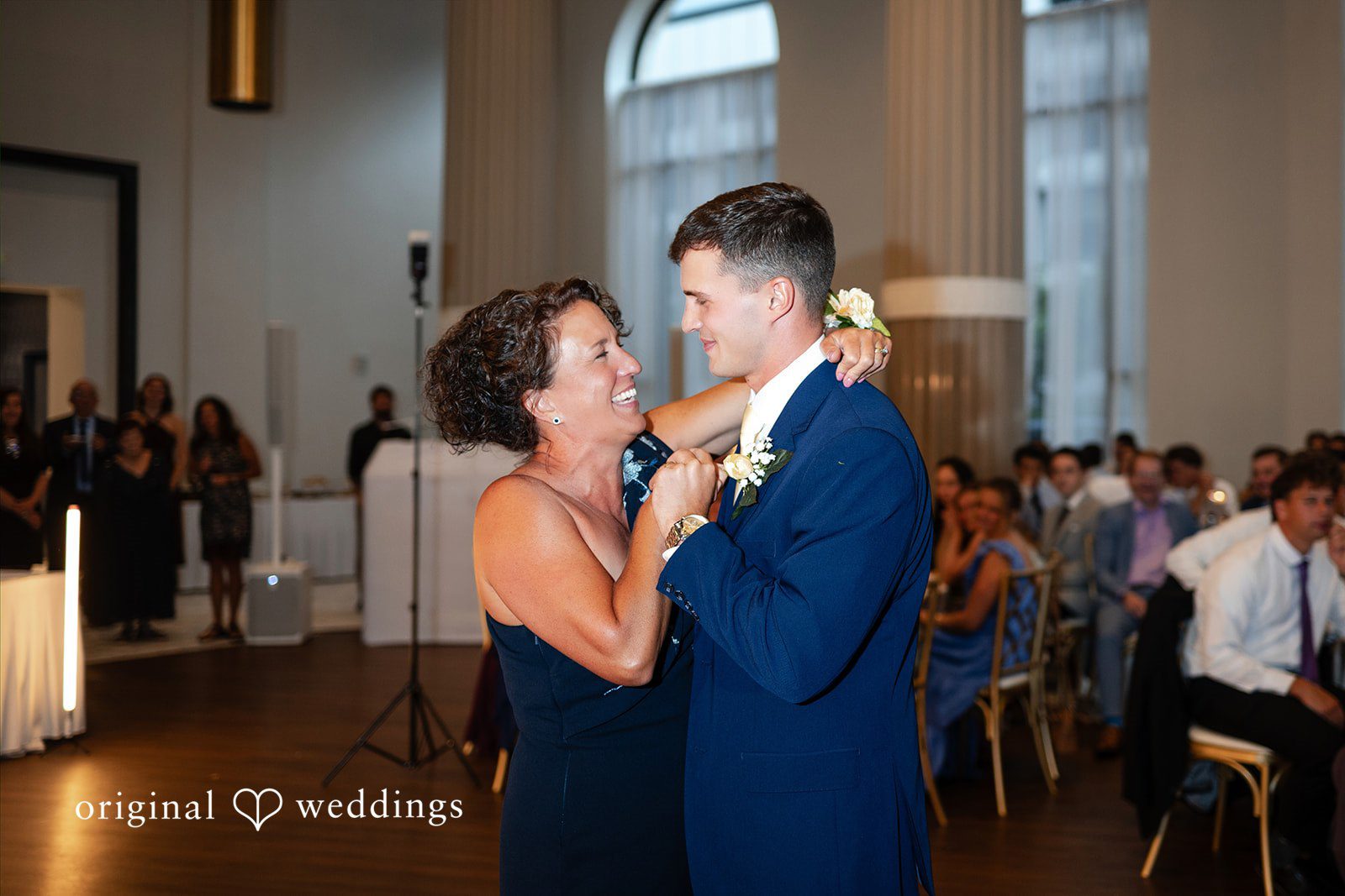 A women and groom dance together while surrounded by guests sitting at reception tables.