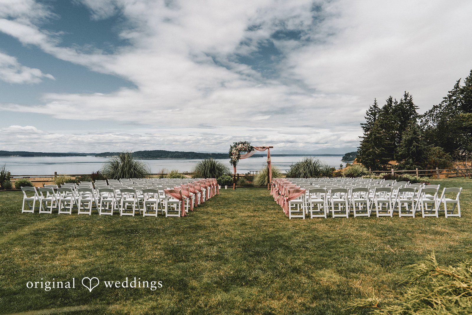 Ashley + Dylan An empty waterfront wedding ceremony setup with white chairs facing a lake.
