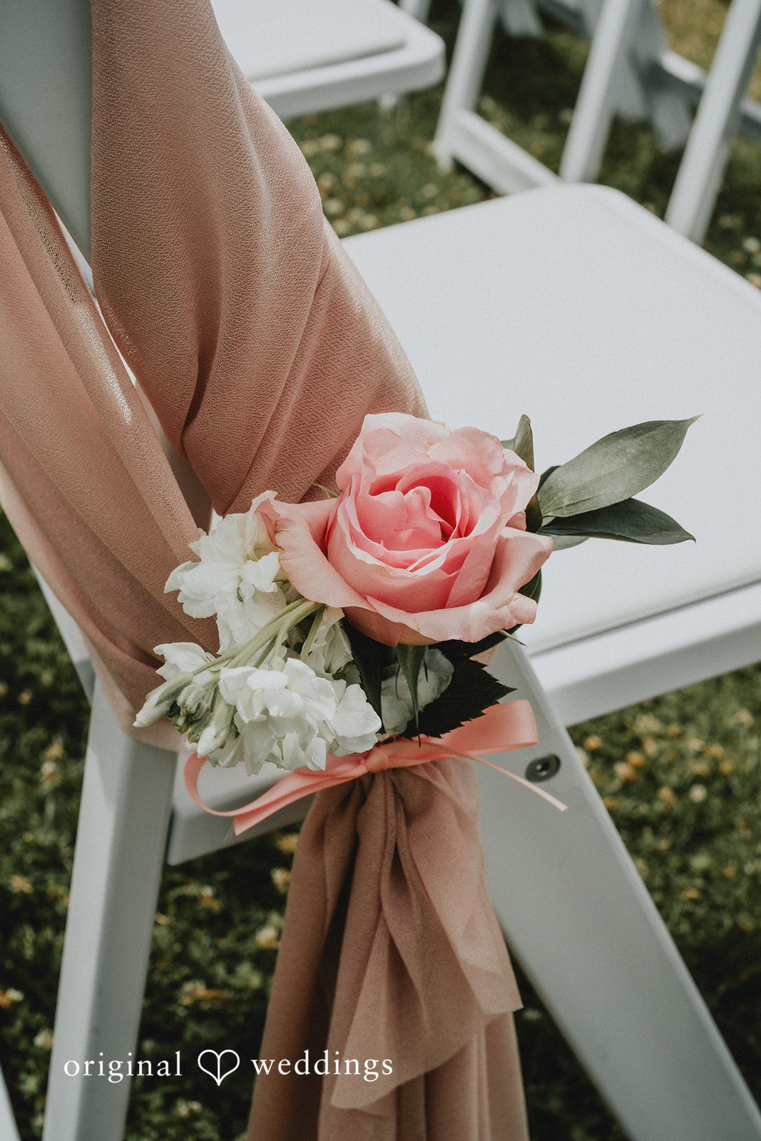 Ashley + Dylan A close-up of a white wedding chair decorated with pink fabric drapery and a rose.