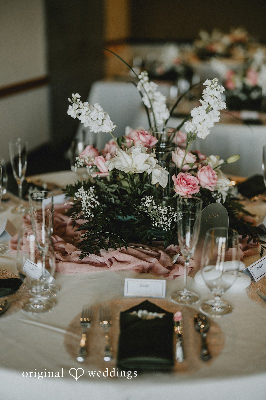 Ashley + Dylan A wedding reception table setting featuring clear glassware, white plates, and lush floral arrangements.