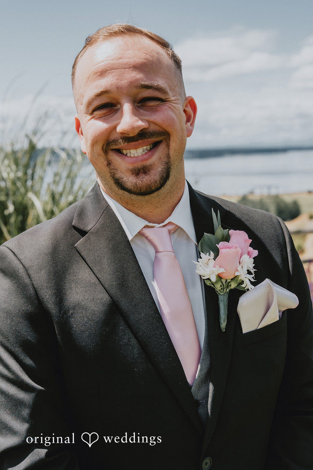 Ashley + Dylan A close-up portrait of a groom in a dark suit smiling widely.