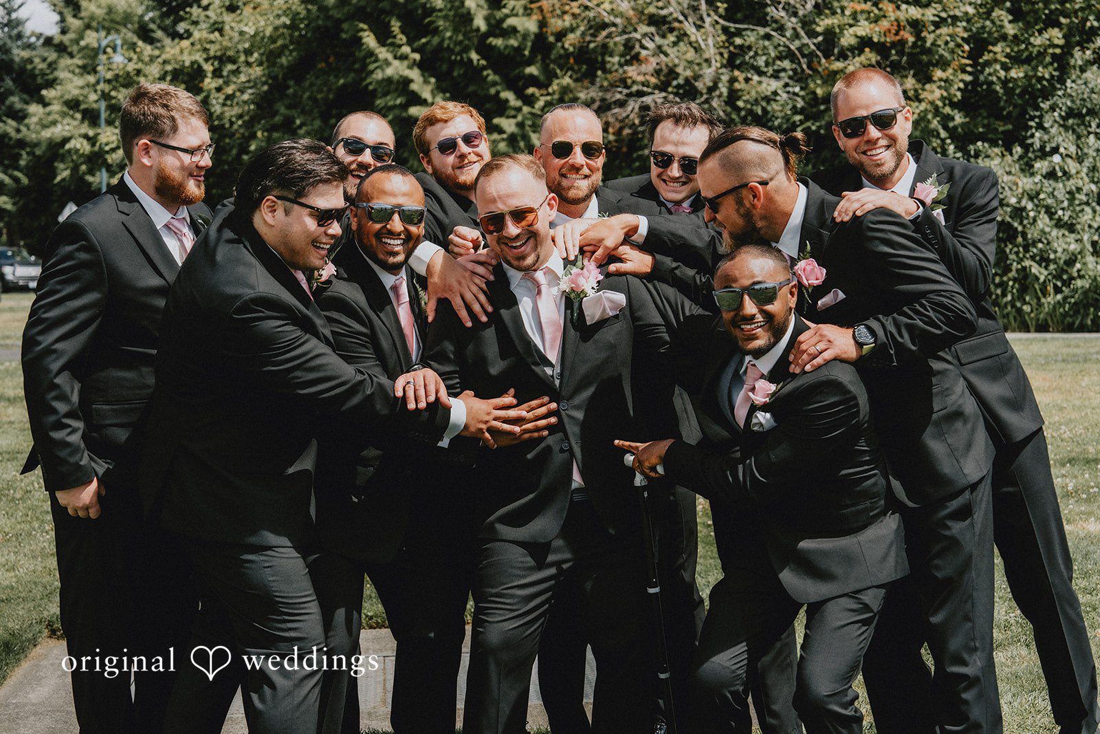Ashley + Dylan A group of groomsmen in black suits celebrating and posing together.