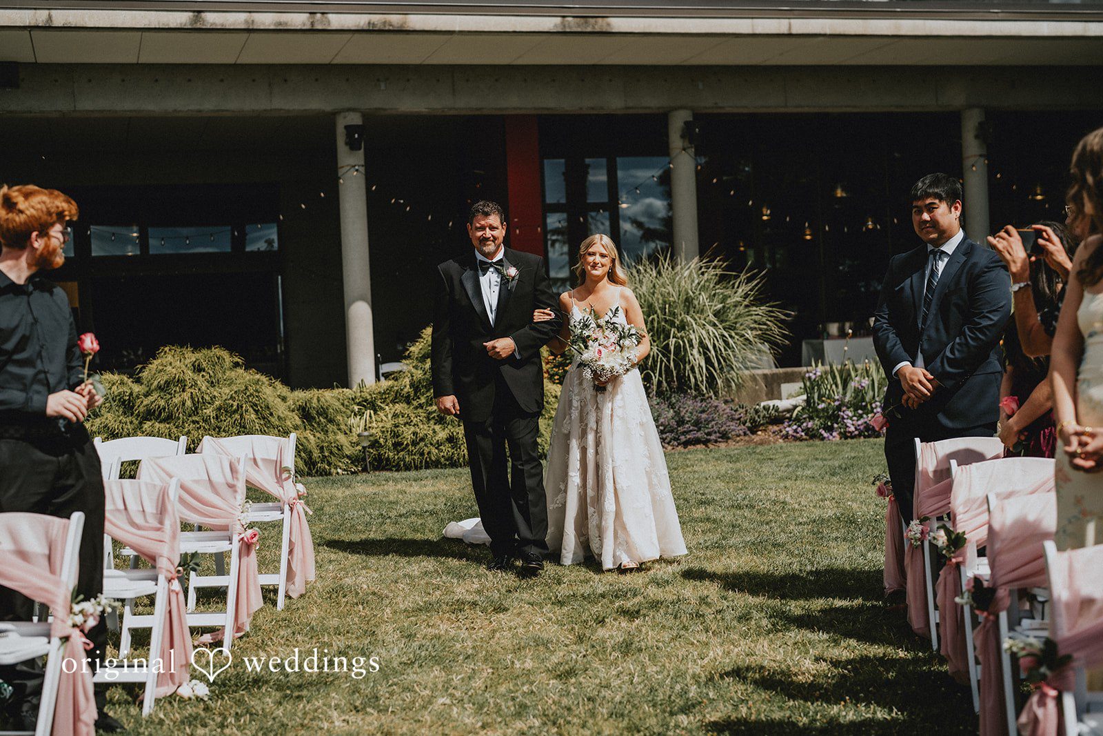 Ashley + Dylan A bride and man walking down a grassy aisle between rows of seated guests.