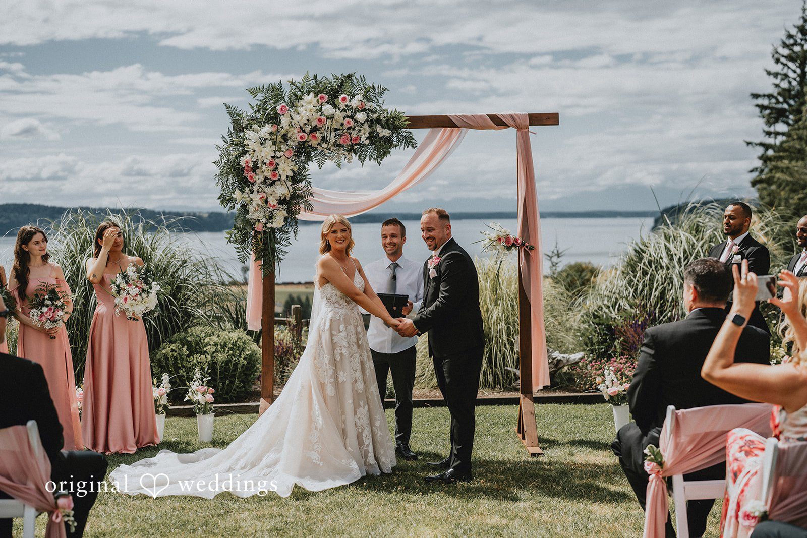 Ashley + Dylan A bride and groom holding hands under a wooden arch during their wedding ceremony.
