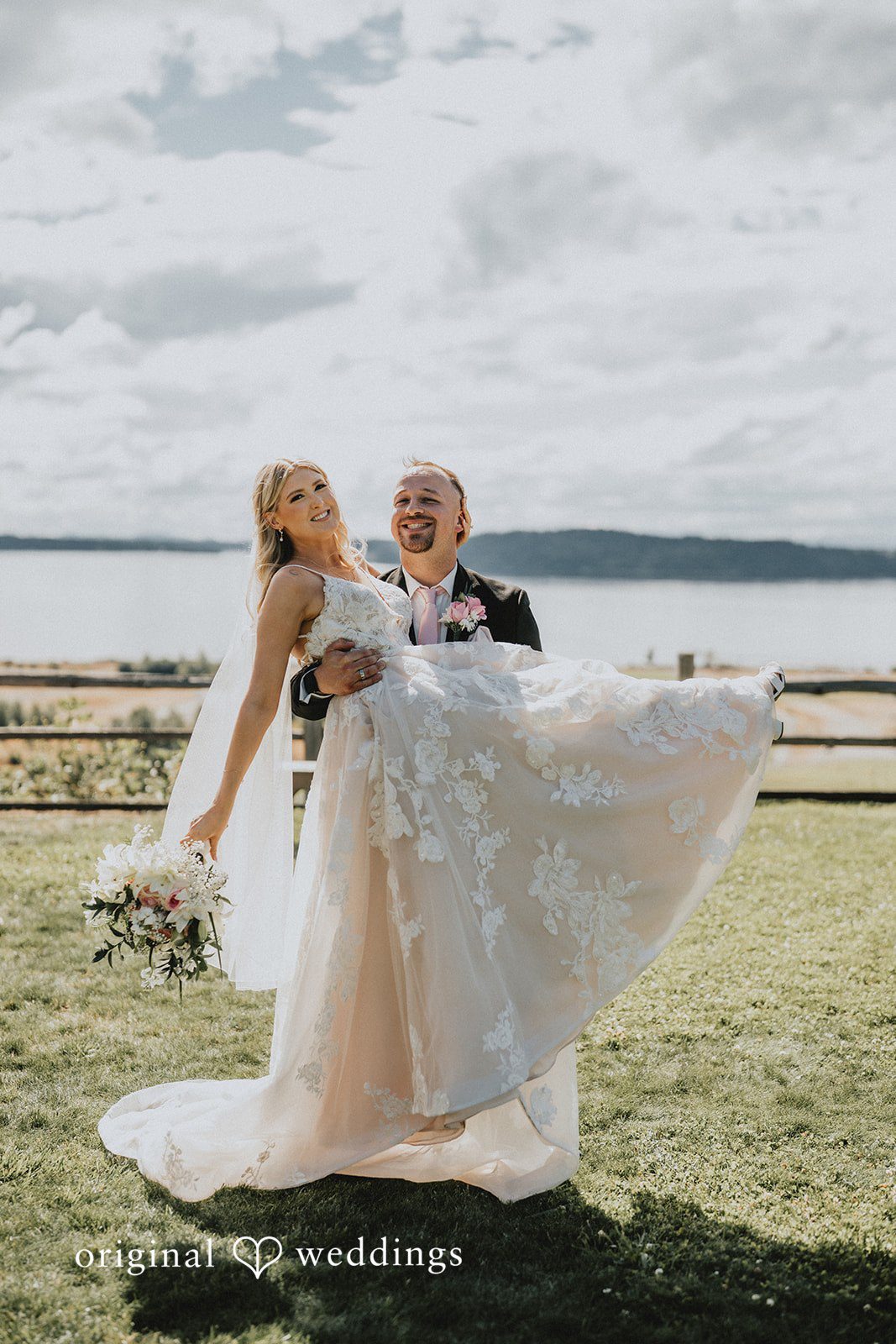 Ashley + Dylan A bride and groom sharing an intimate embrace on a grassy field near the water.