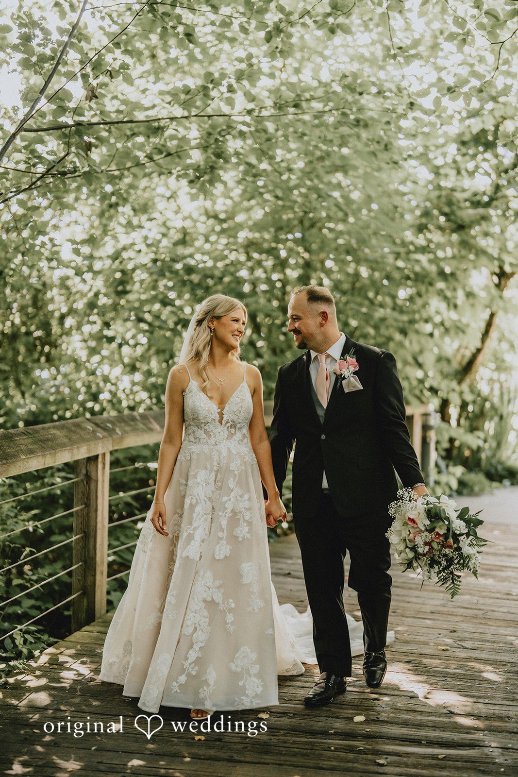 Ashley + Dylan A bride and groom walking down a path surrounded by lush trees.